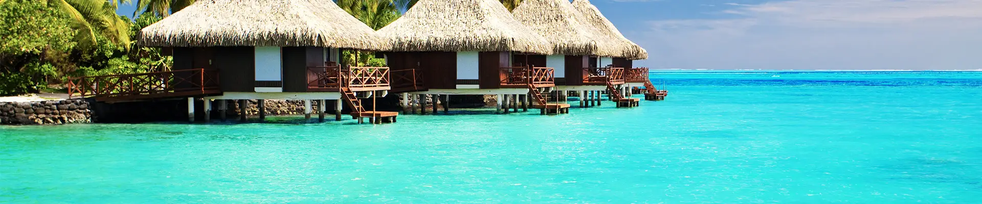 Three huts on the shore surrounded by crystal clear blue water