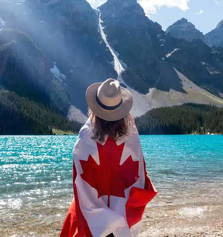 A woman wrapped in a canadian flag on the shore of a lake in Canada