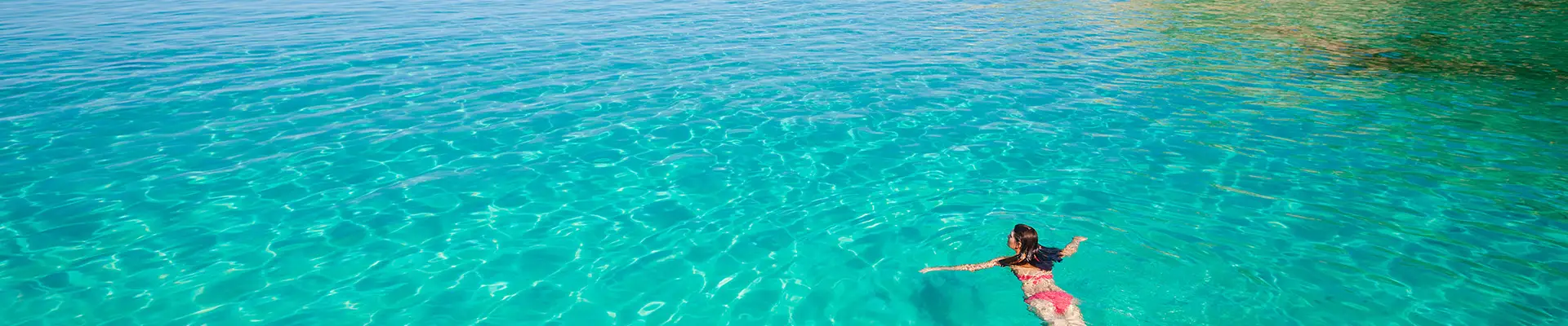 A woman swimming through crystal clear water with a cliff in view