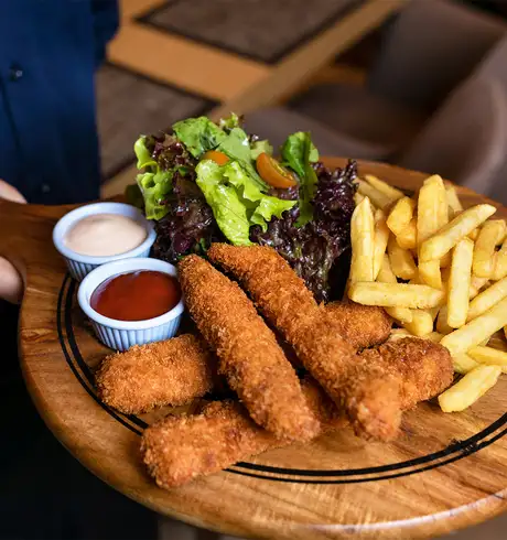 A plate of Chicken, Chips, Vegetables and sauces carried by a server