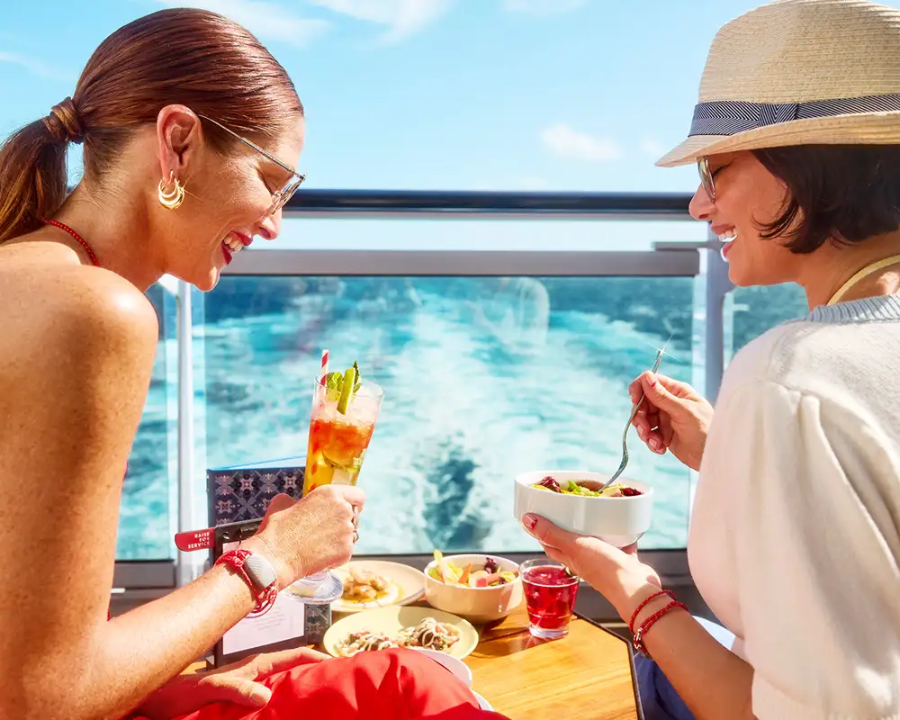 Two women enjoying some food and drinks while looking over the ocean