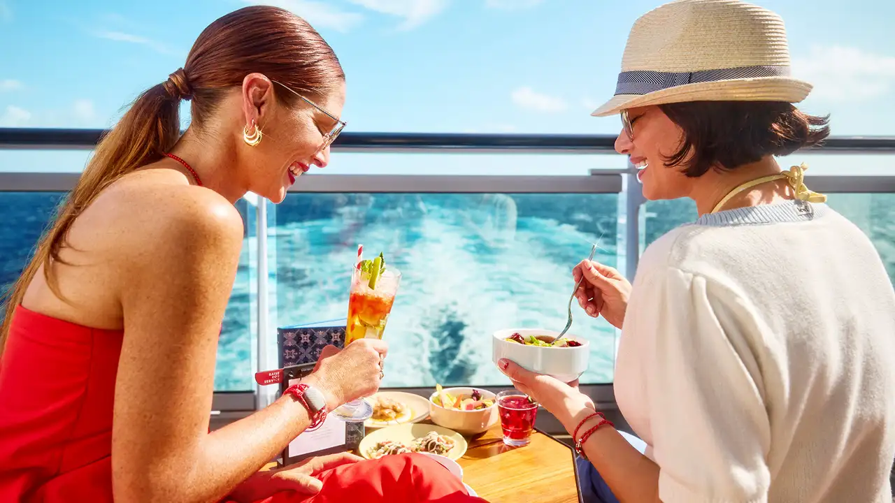 Two women enjoying some food and drinks while looking over the ocean