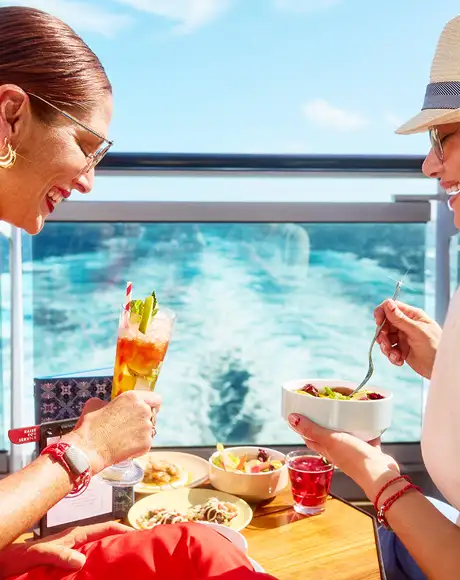 Two women enjoying some food and drinks while looking over the ocean