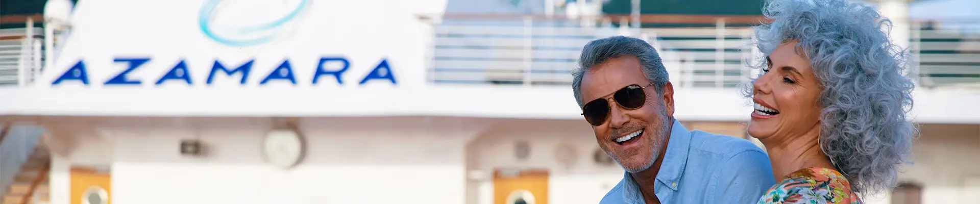 A couple enjoying drinks, leaning on a railing aboard an Azamara Cruise Ship