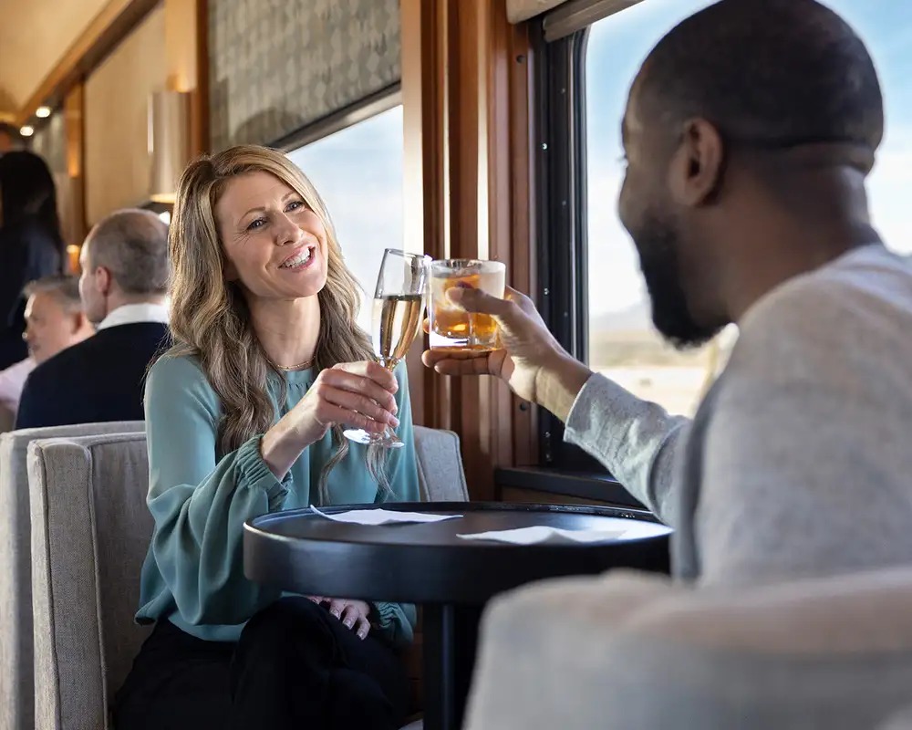 A couple cheering drinks on the Rocky Mountaineer as part of the Silver Leaf Plus package
