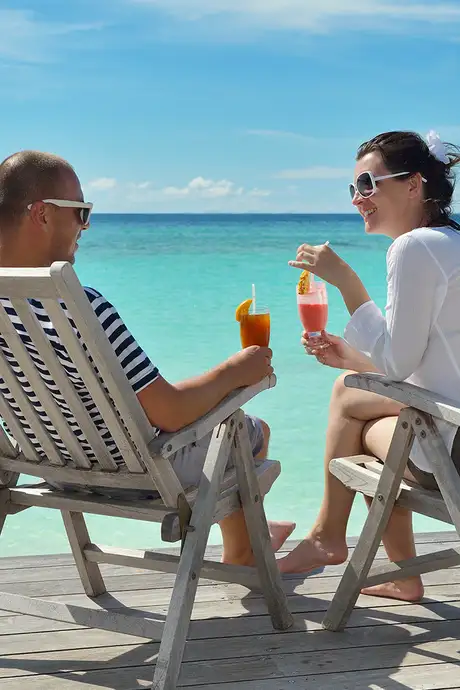 A couple sipping on drinks while sitting in chairs near the ocean