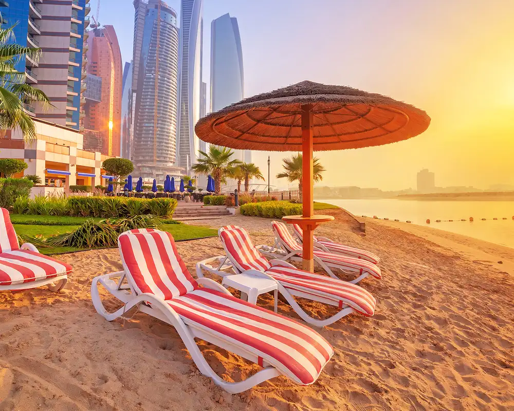 A beach in Dubai at sunset with red and white striped lounge chairs near the ocean