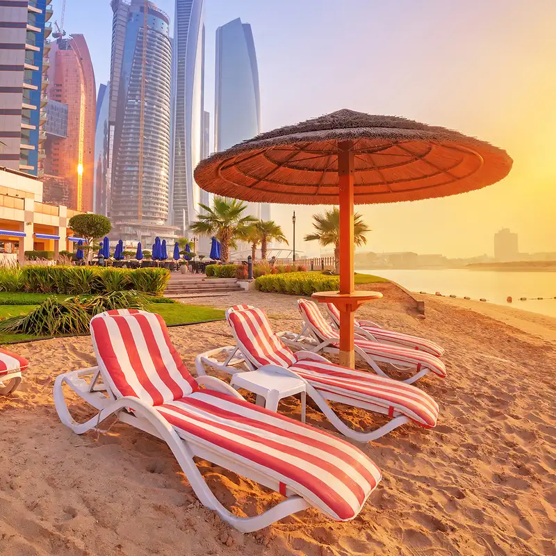 A beach in Dubai at sunset with red and white striped lounge chairs near the ocean