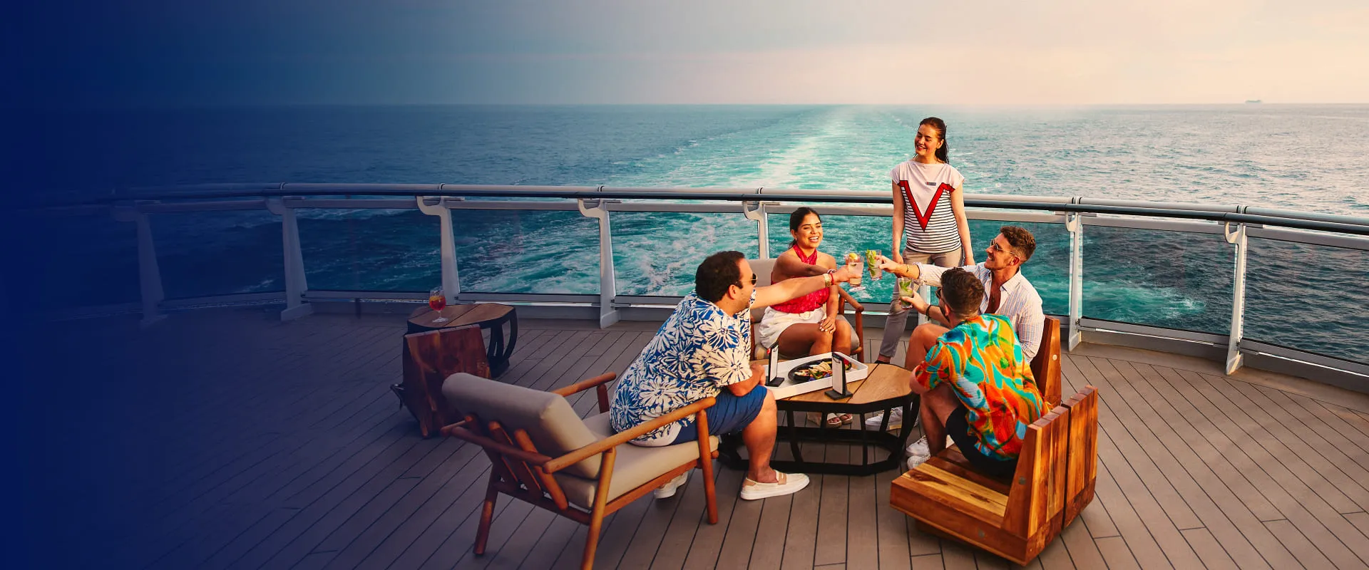 A group of people enjoys a toast on a cruise ship deck, with the ocean and a sunny horizon in the background.