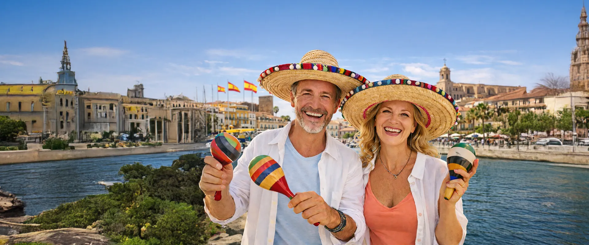 A smiling couple in straw hats playing maracas by a waterfront, with historic buildings and Spanish flags in the background.