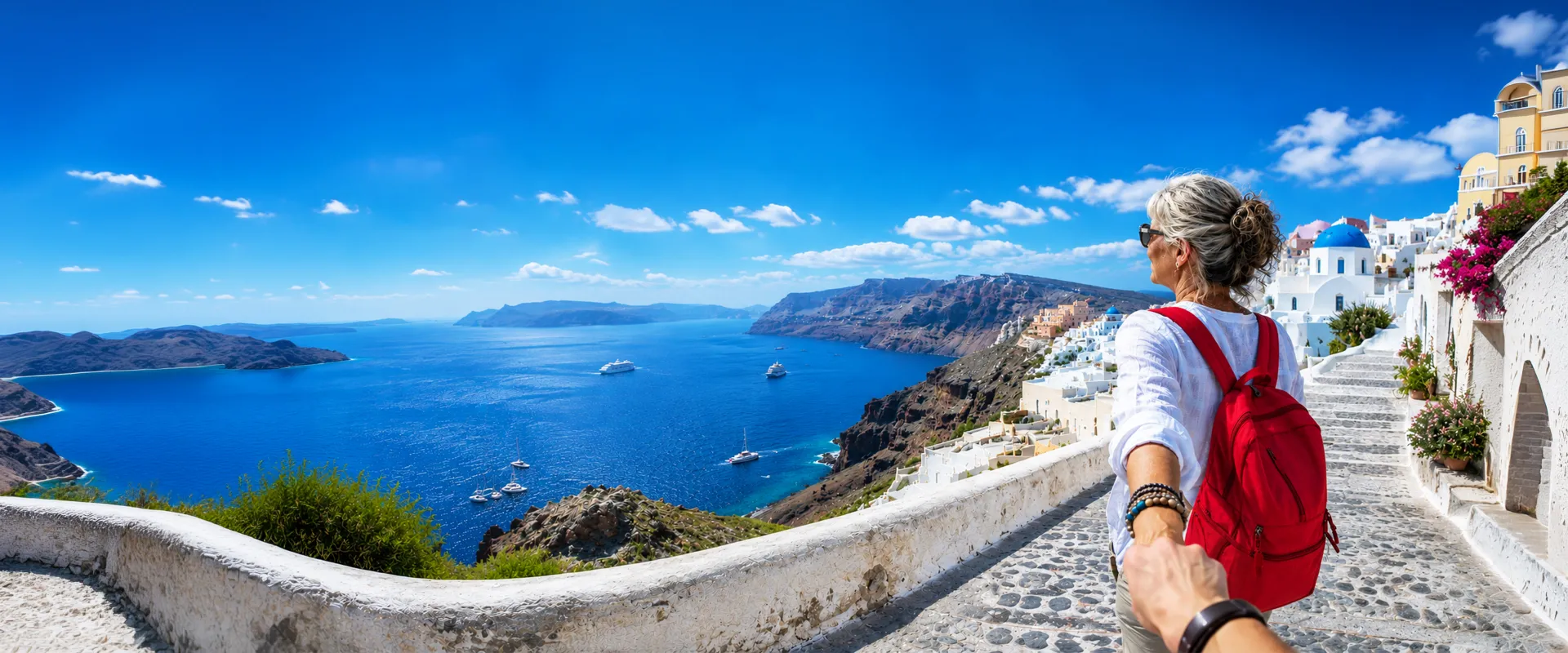 Woman with a red backpack leads the viewer down a scenic path overlooking Santorini's blue sea and white buildings.
