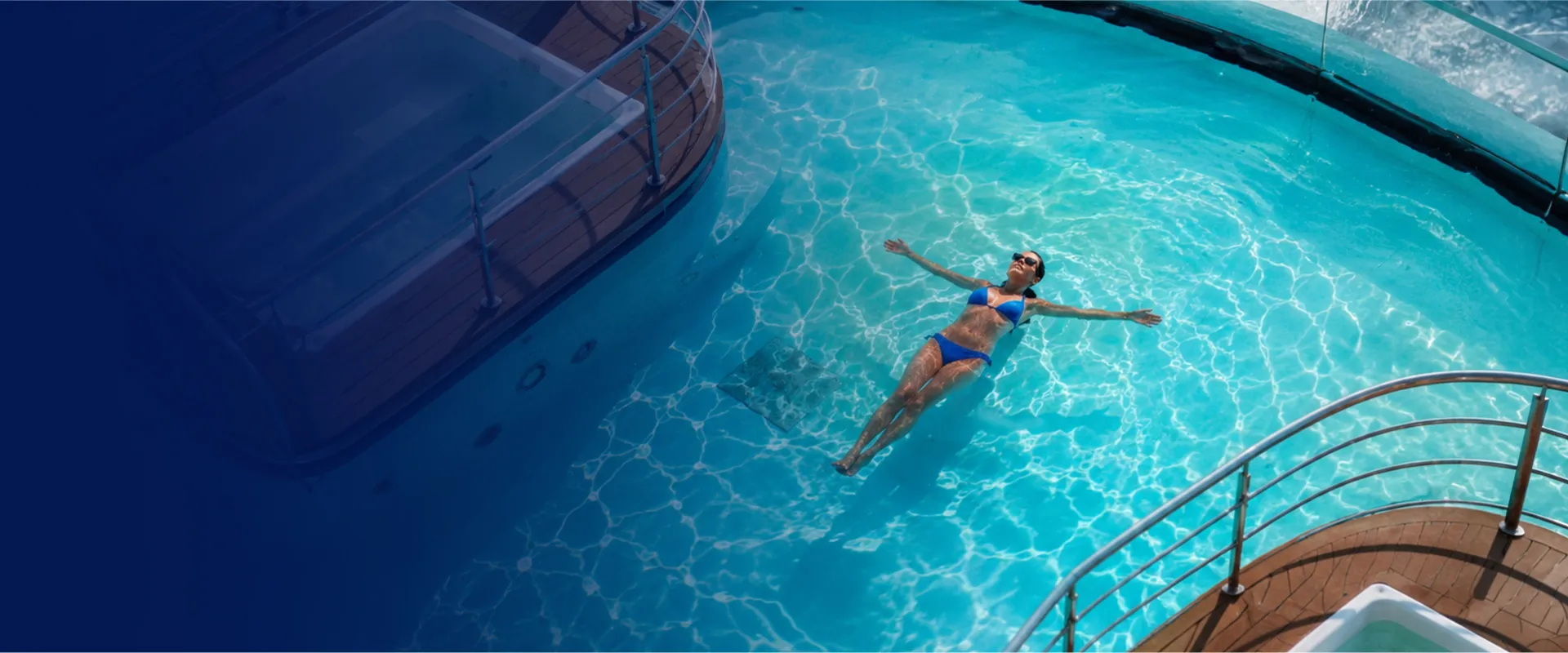 A person in a blue swimsuit floats peacefully in a clear pool, surrounded by a yacht's wooden deck railing.