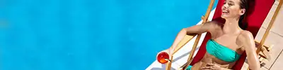A woman lay on a deck chair near a pool holding a cocktail