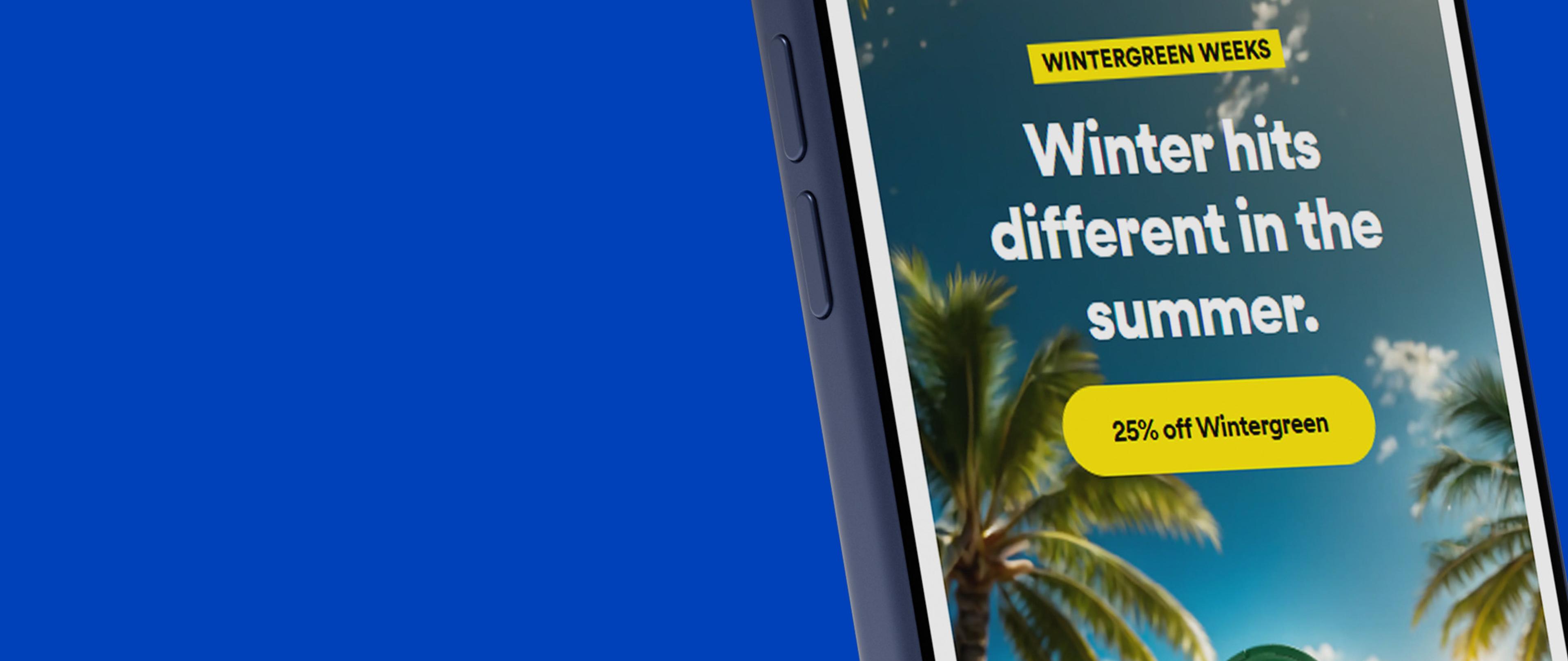Smartphone screen showing an ad: "Winter hits different in the summer. 25% off Wintergreen," with palm trees in the background.