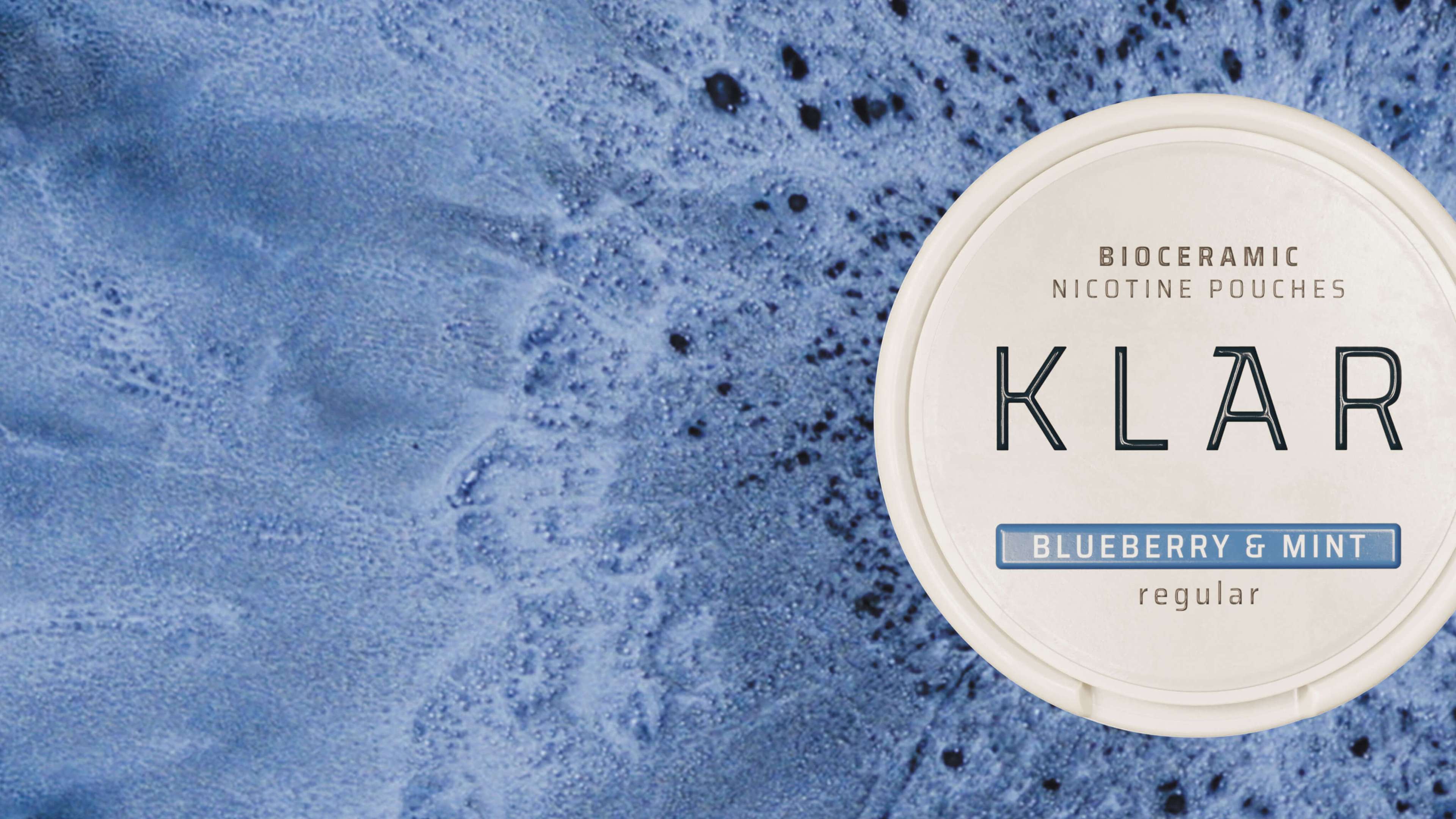A round container of bioceramic nicotine pouches labeled "KLAR Blueberry & Mint Regular" on a textured blue background.