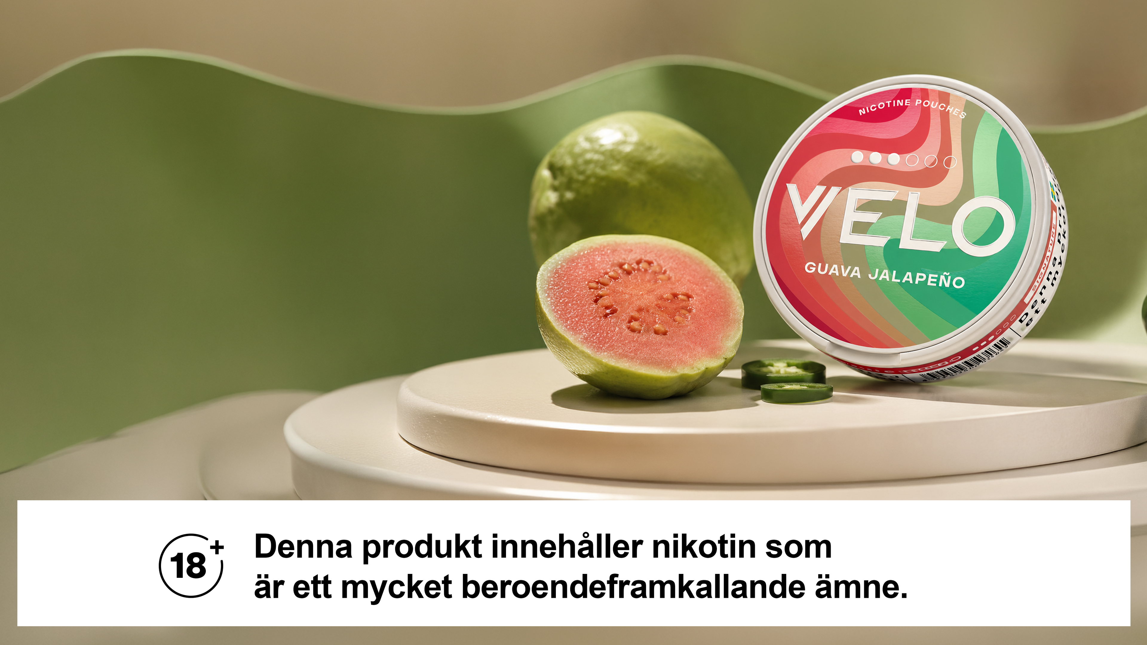 A colorful Velo nicotine pouch labeled "Guava Jalapeño" next to sliced guava and jalapeño, with a warning for 18+ users in Swedish.
