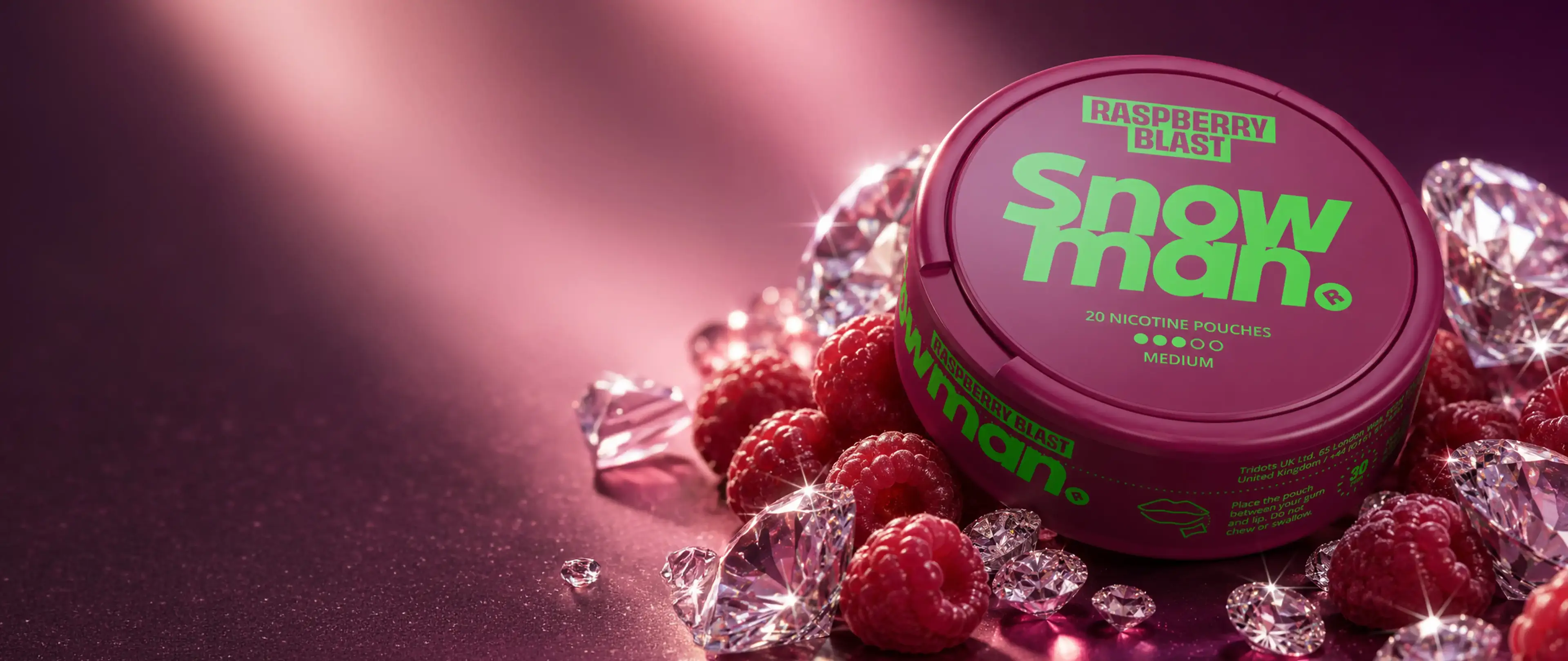 Round raspberry-colored tin labeled "Snowman Raspberry Blast" surrounded by raspberries and sparkling gems on a pink surface.