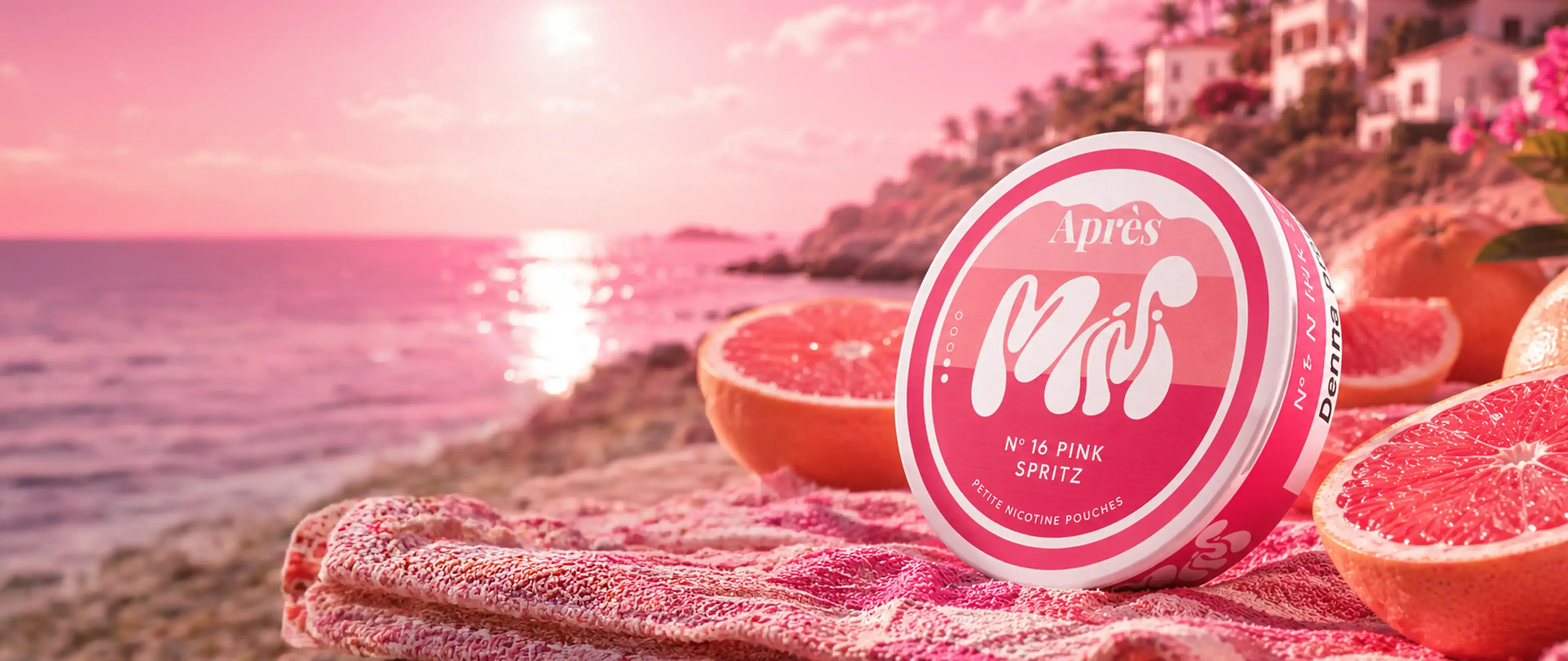 Pink tin labeled "Après No. 16 Pink Spritz" on a towel with grapefruit slices by a seaside at sunset.
