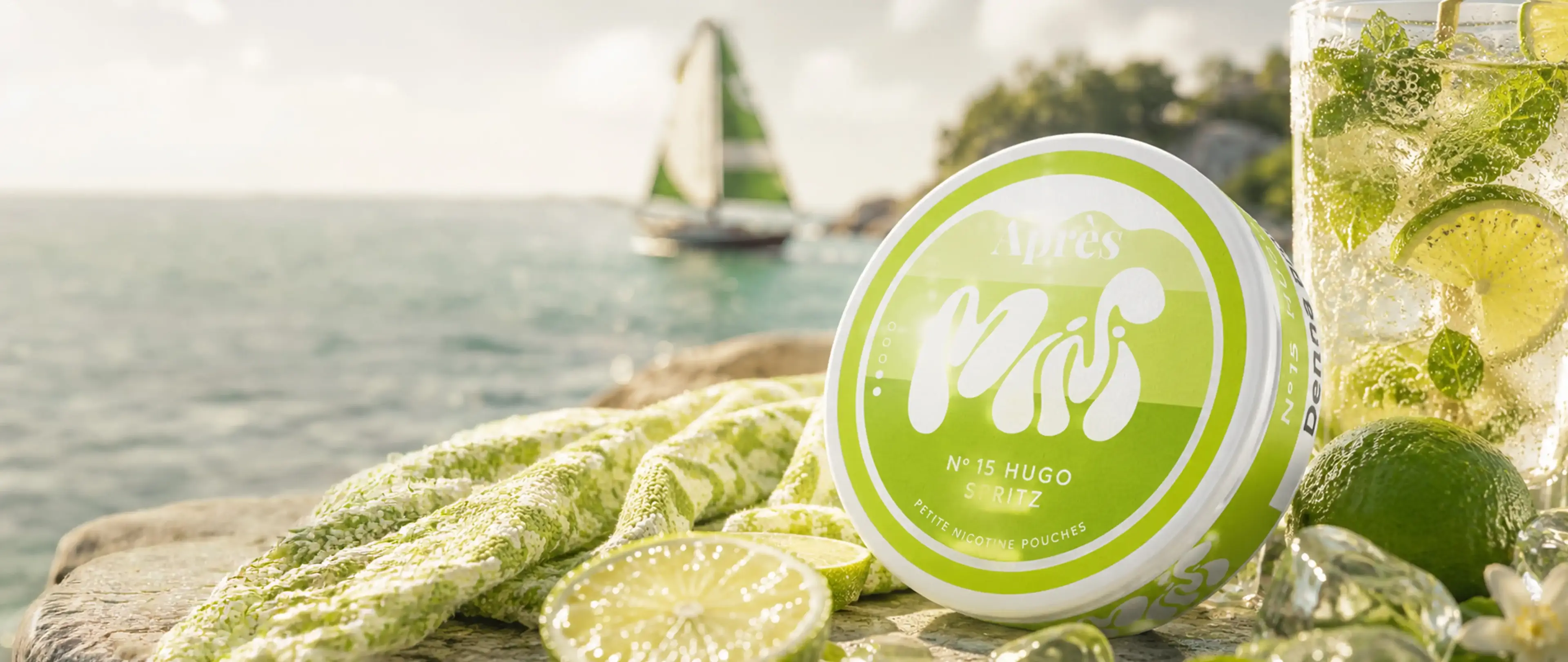 Green nicotine pouches with sliced lime and drink by the sea; blurred sailboat in the background.