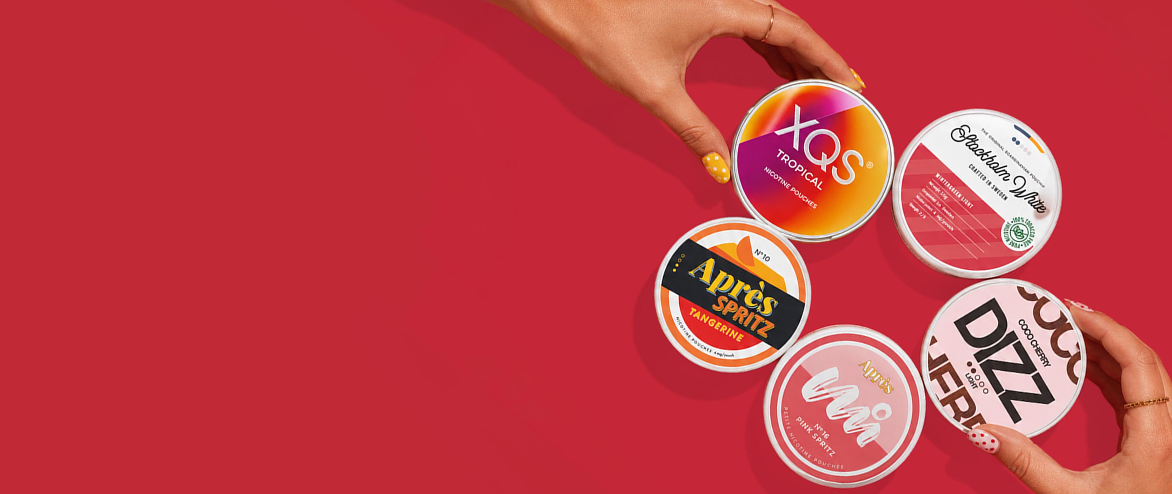 Five colorful nicotine pouch tins on a red background, with hands holding two of them.