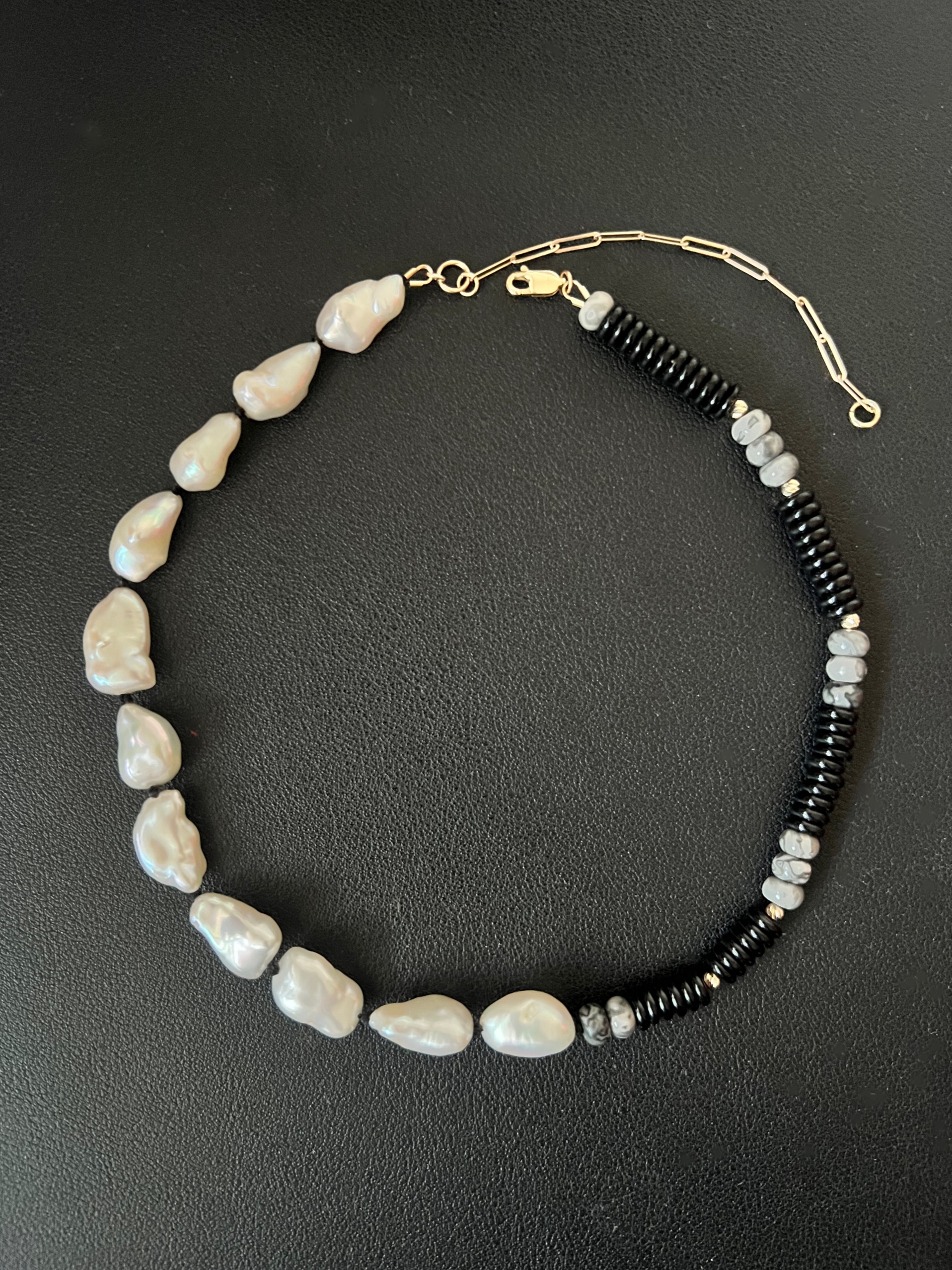 A necklace with irregular white pearls on one side and alternating black and gray beads on the other, against a black background.