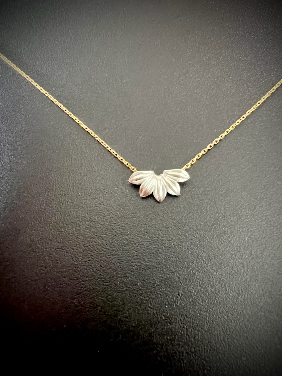 Gold necklace with a delicate chain and a pendant shaped like three overlapping leaves, set against a black background.