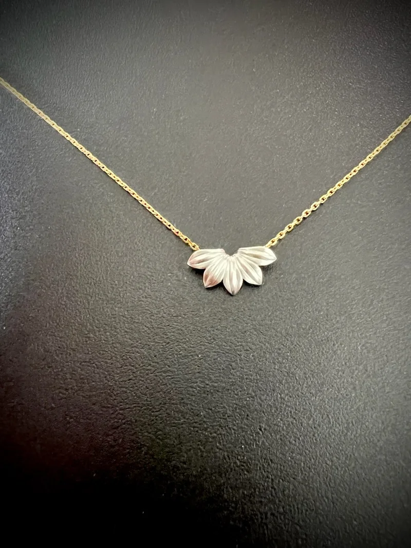 Gold necklace with a delicate chain and a pendant shaped like three overlapping leaves, set against a black background.