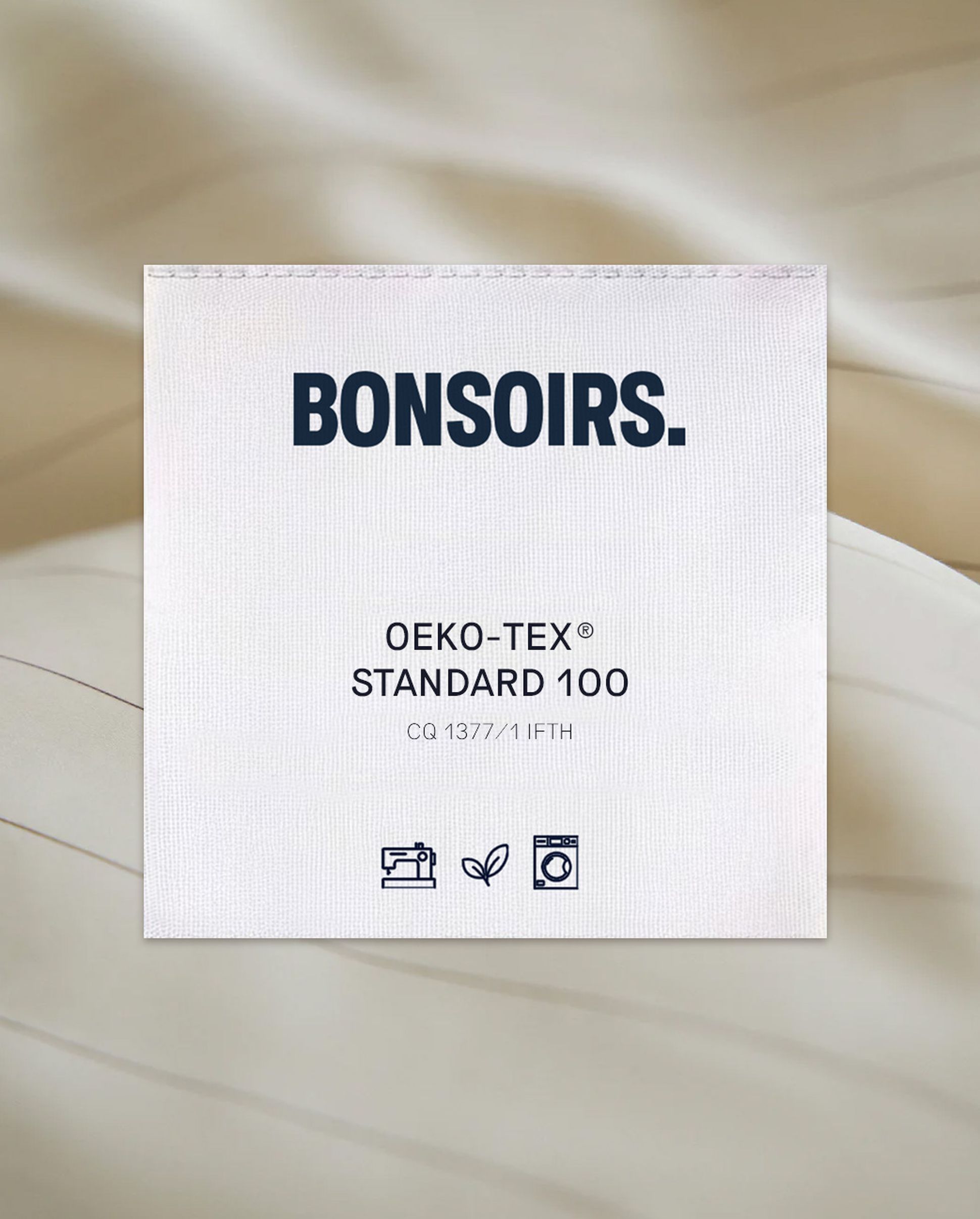 Étiquette en tissu portant la mention « BONSOIRS », « OEKO-TEX STANDARD 100 », des symboles indiquant les consignes de lavage et le respect de l'environnement, ainsi qu'un code d'identification.