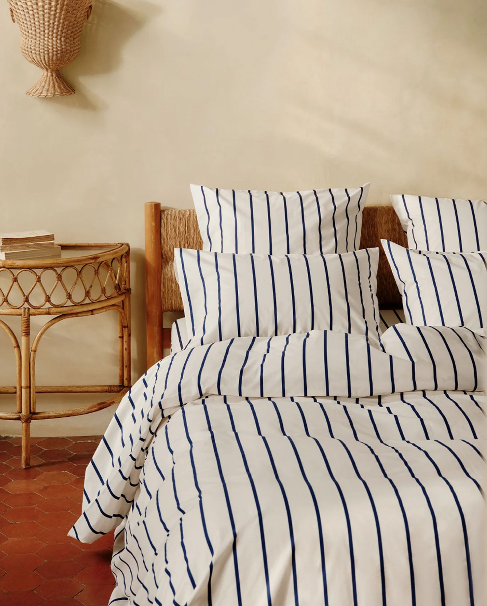 A bed with blue and white striped bedding, surrounded by wicker furniture and soft beige walls, creating a cozy, natural ambiance.
