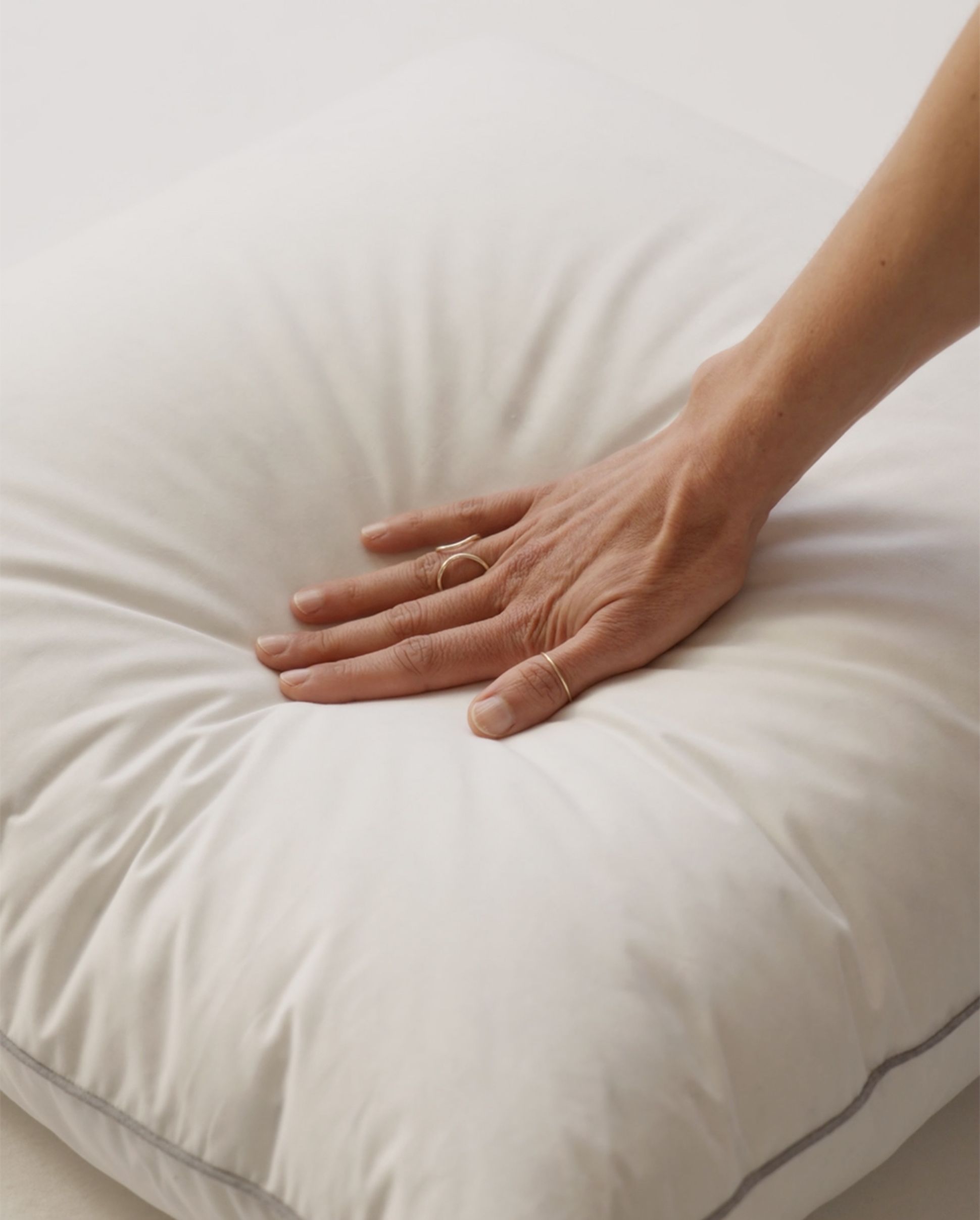 Une main de femme avec une bague qui se pose sur un oreiller pour en tester le confort