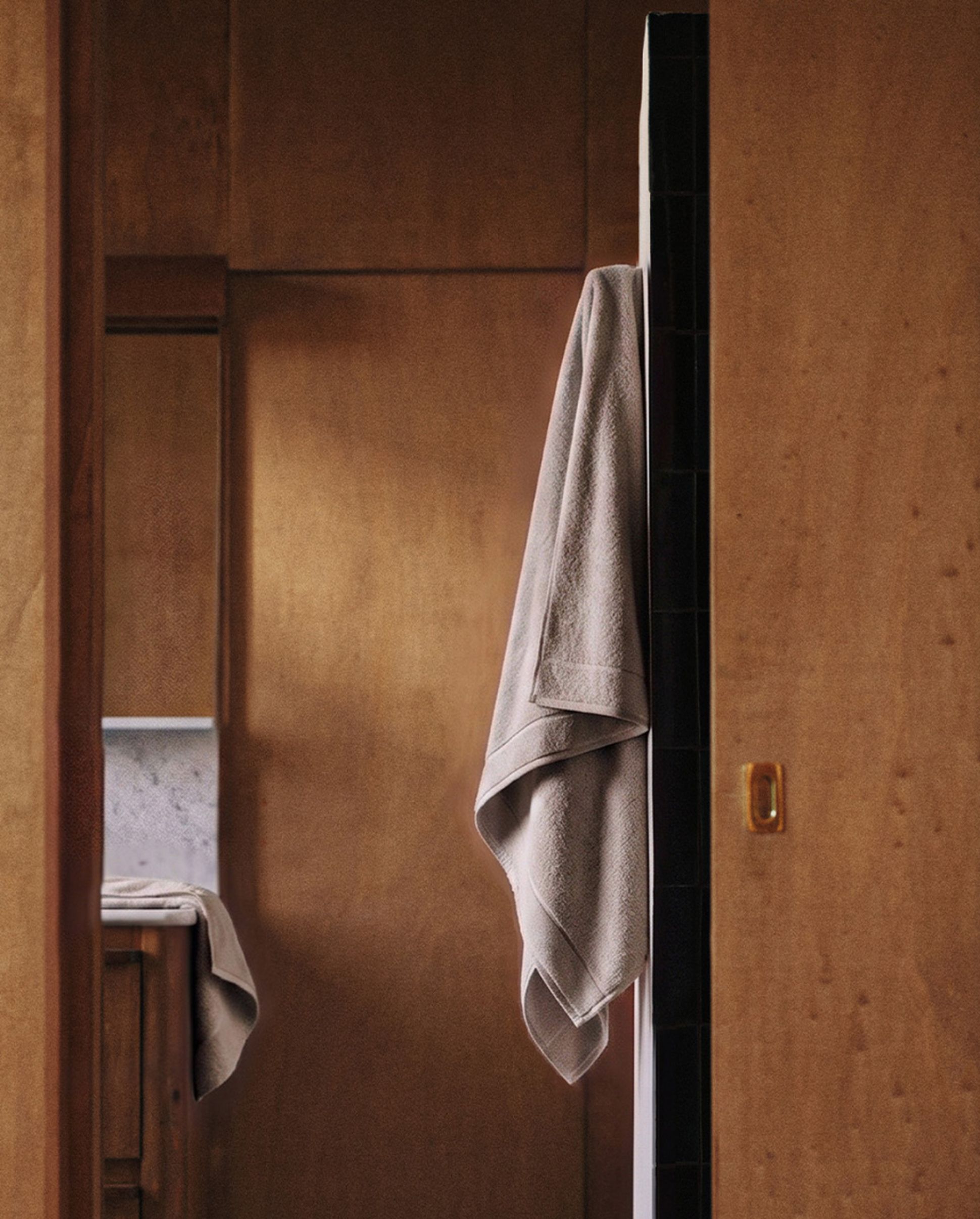 A beige towel hangs on a wooden bathroom door, with a glimpse of a sink and countertop in the background.