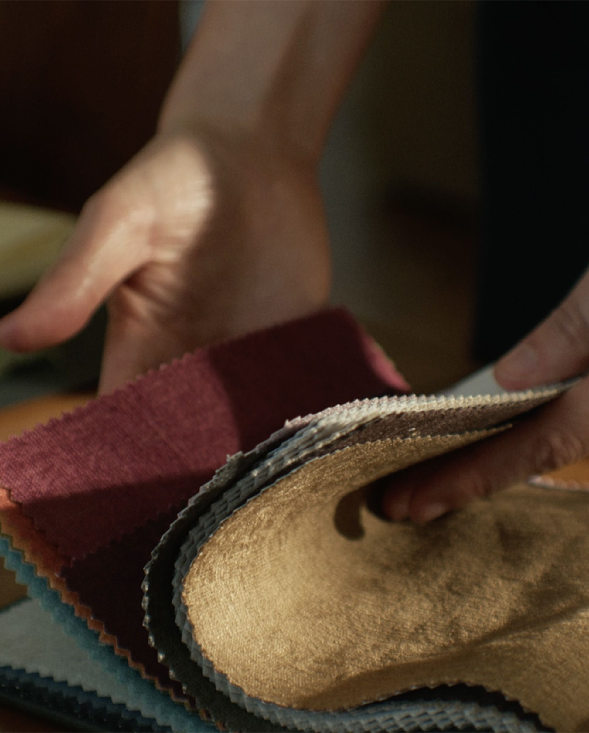 Des mains tenant une sélection d'échantillons de tissus de différentes couleurs et textures, posés sur une surface en bois.