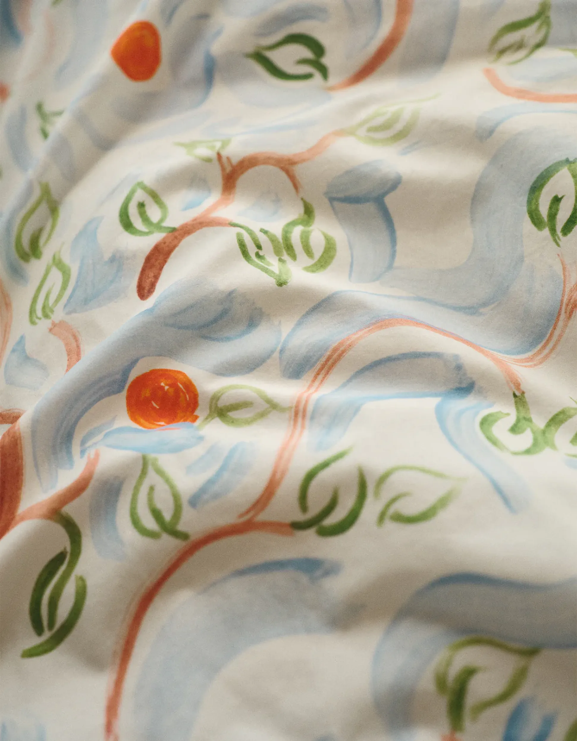 Gros plan sur des coussins au motif abstrait composé de lignes courbes bleues, vertes et orange, rehaussés d'un liseré orange.