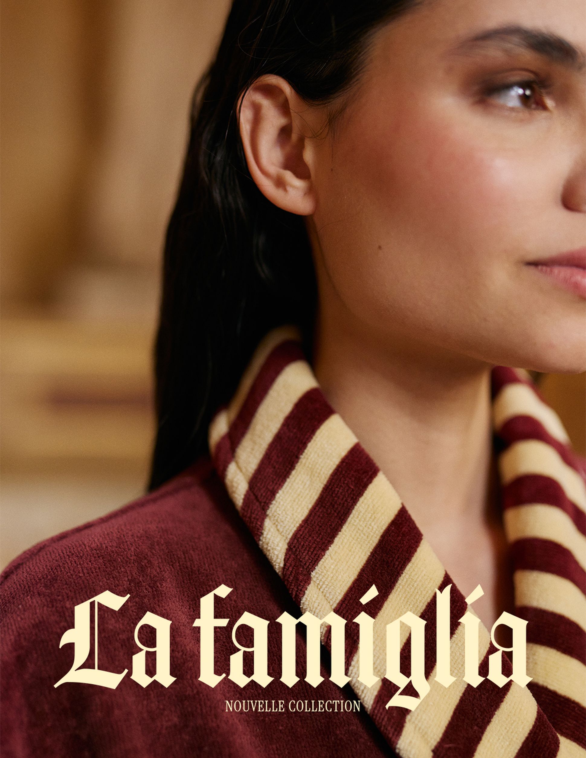 Gros plan sur une femme vêtue d'un peignoir rayé bordeaux et crème, sur lequel apparaissent les inscriptions « La famiglia » et « New Collection ».