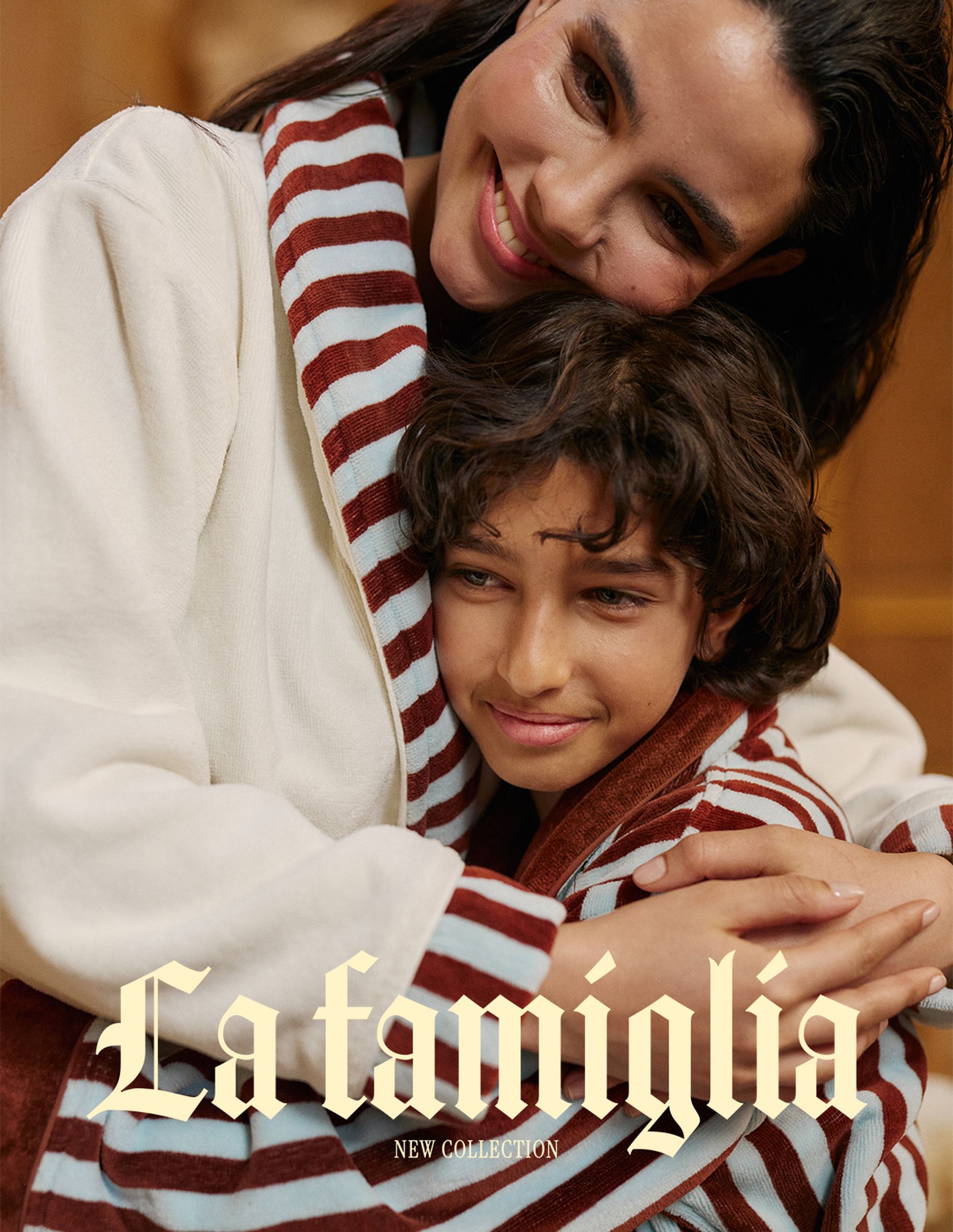 Une femme et un enfant souriants, vêtus de tenues rayées assorties, s'étreignent chaleureusement ; le texte indique « La famiglia New Collection ».