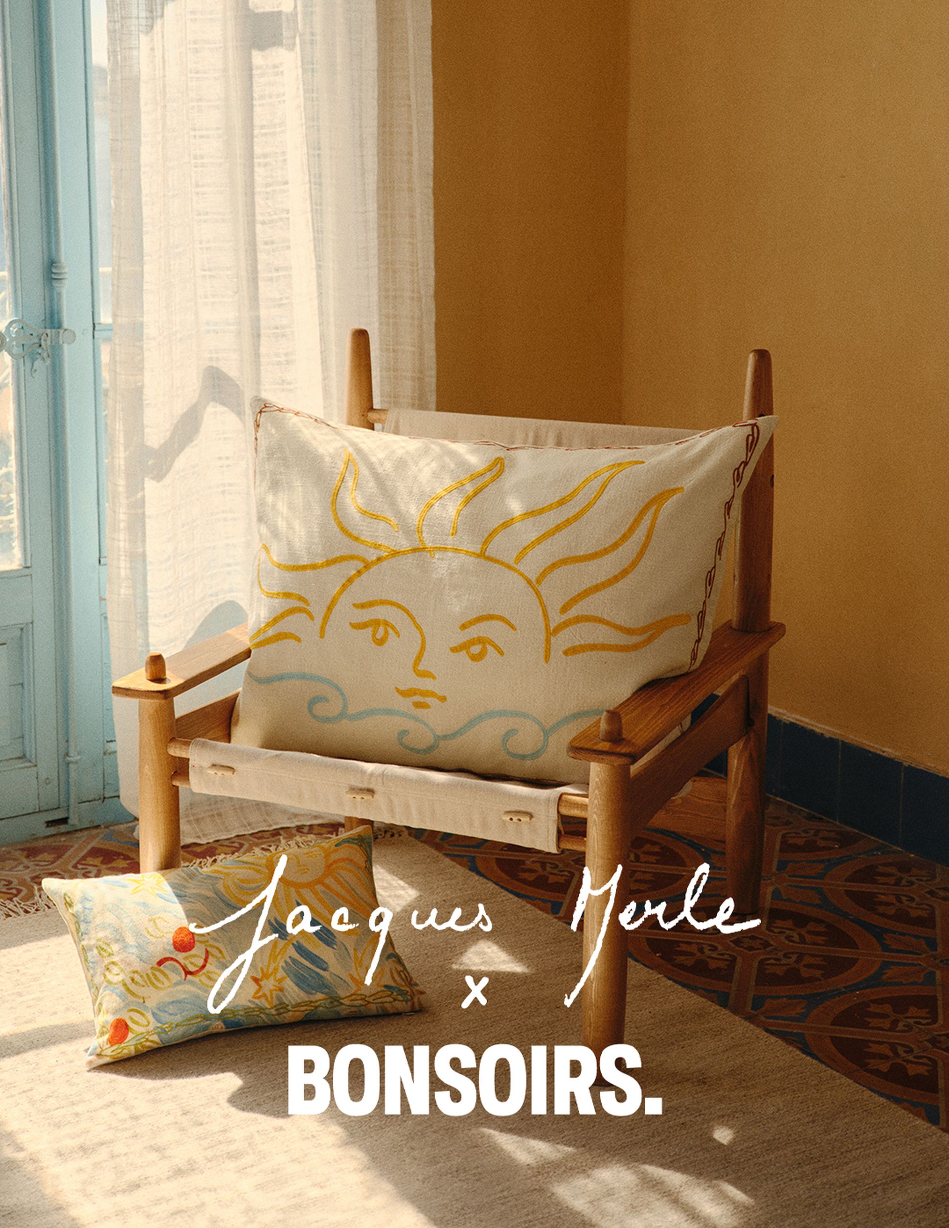 Chaise en bois avec un coussin représentant un soleil et des vagues, un oreiller à motifs et l'inscription « Jacques Merle x BONSOIRS » dans une pièce lumineuse et chaleureuse.