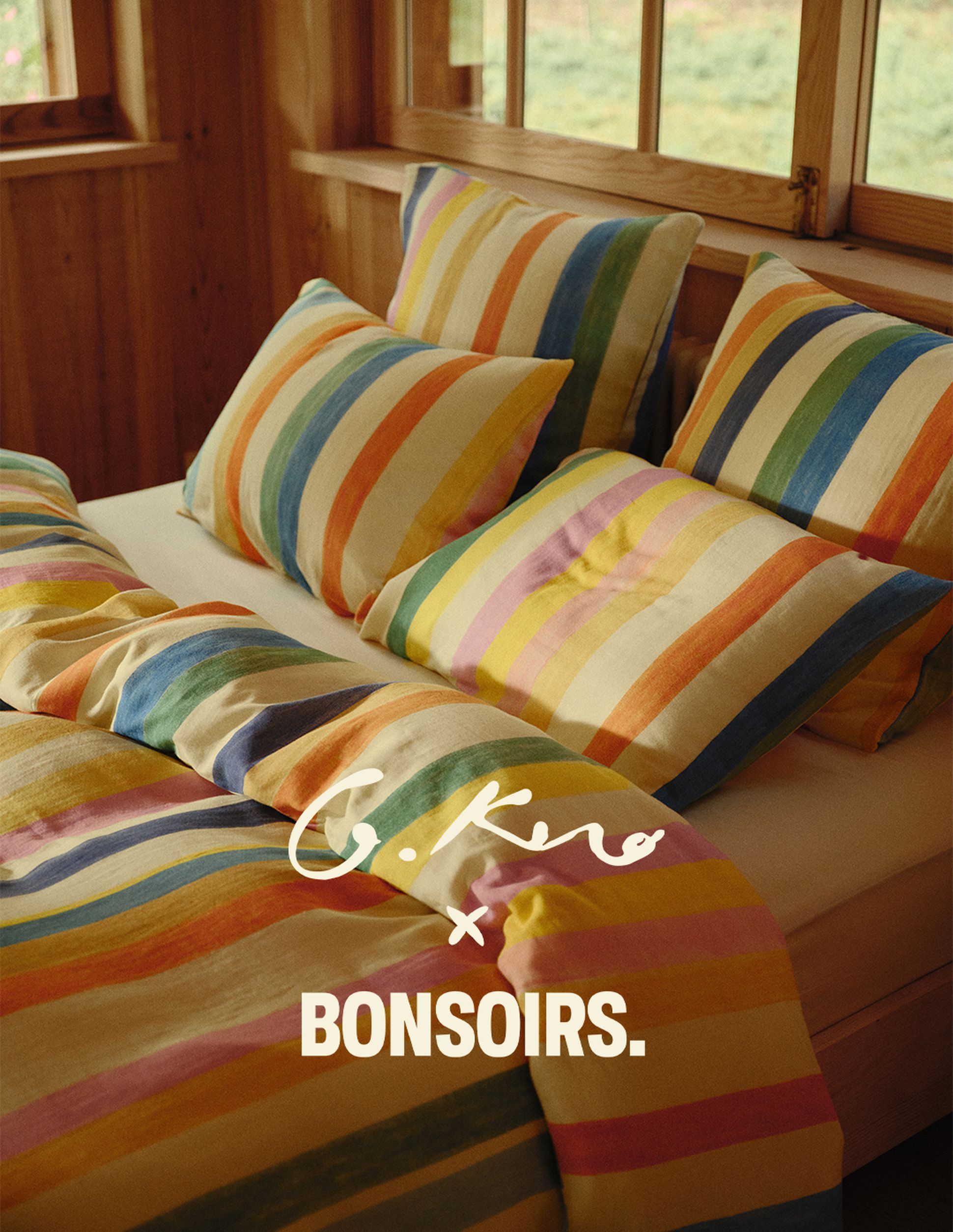 Un lit douillet avec une parure de lit à rayures colorées dans une chambre en bois, fruit d'une collaboration entre G.Kero et Bonsoirs