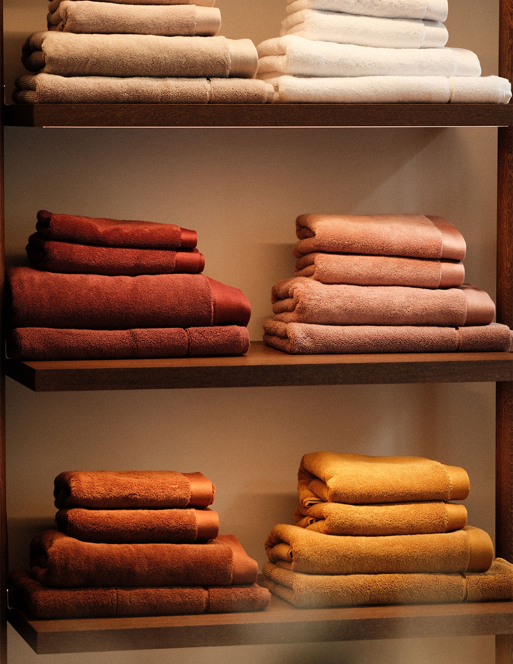 Des étagères sur lesquelles sont soigneusement empilées des serviettes dans diverses teintes chaudes, notamment le marron, l'orange et le beige.