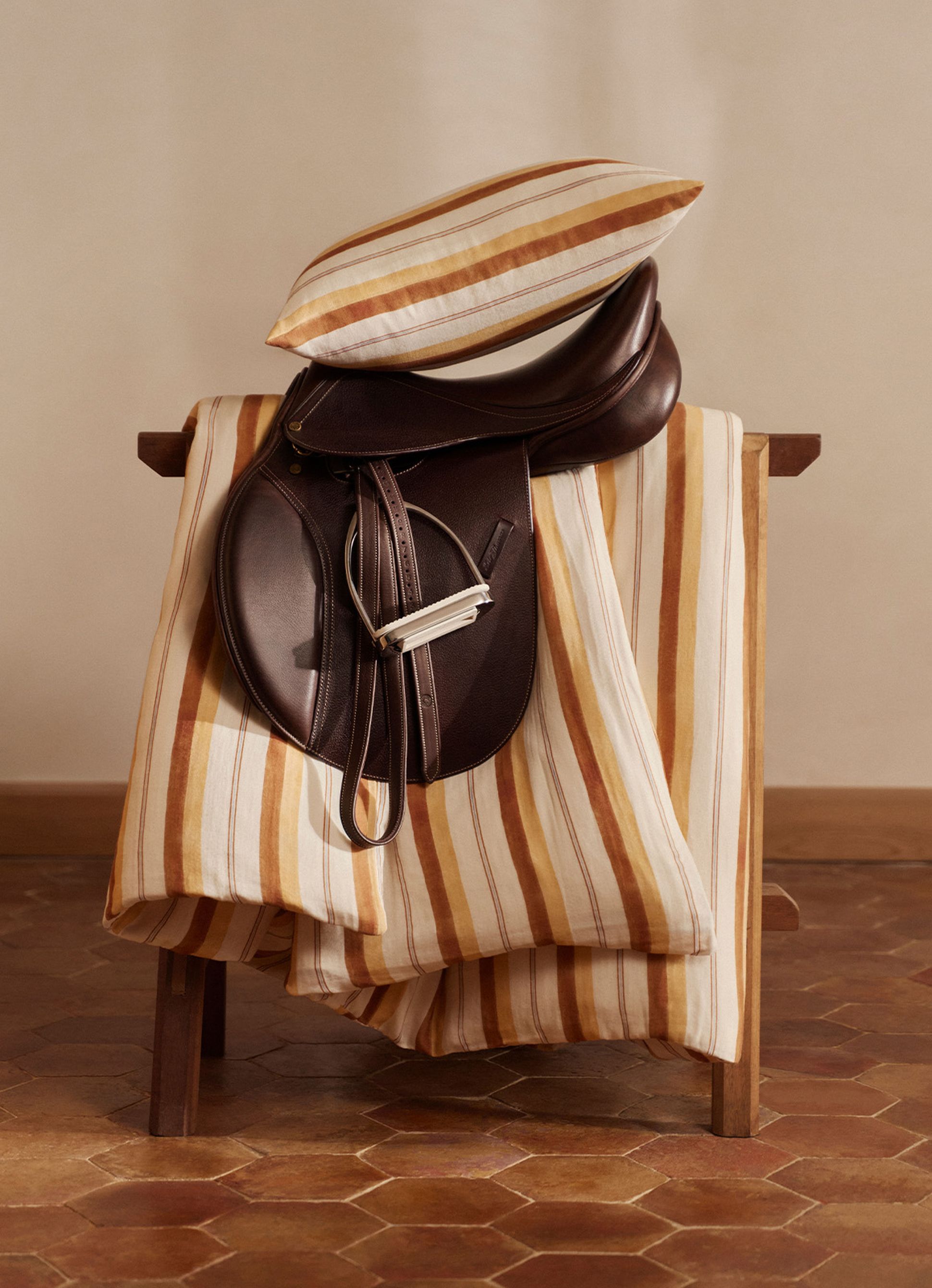 Une chaise en bois recouverte d'un tissu rayé et d'une selle en cuir foncé, surmontée d'un coussin rayé, posée sur un sol carrelé.