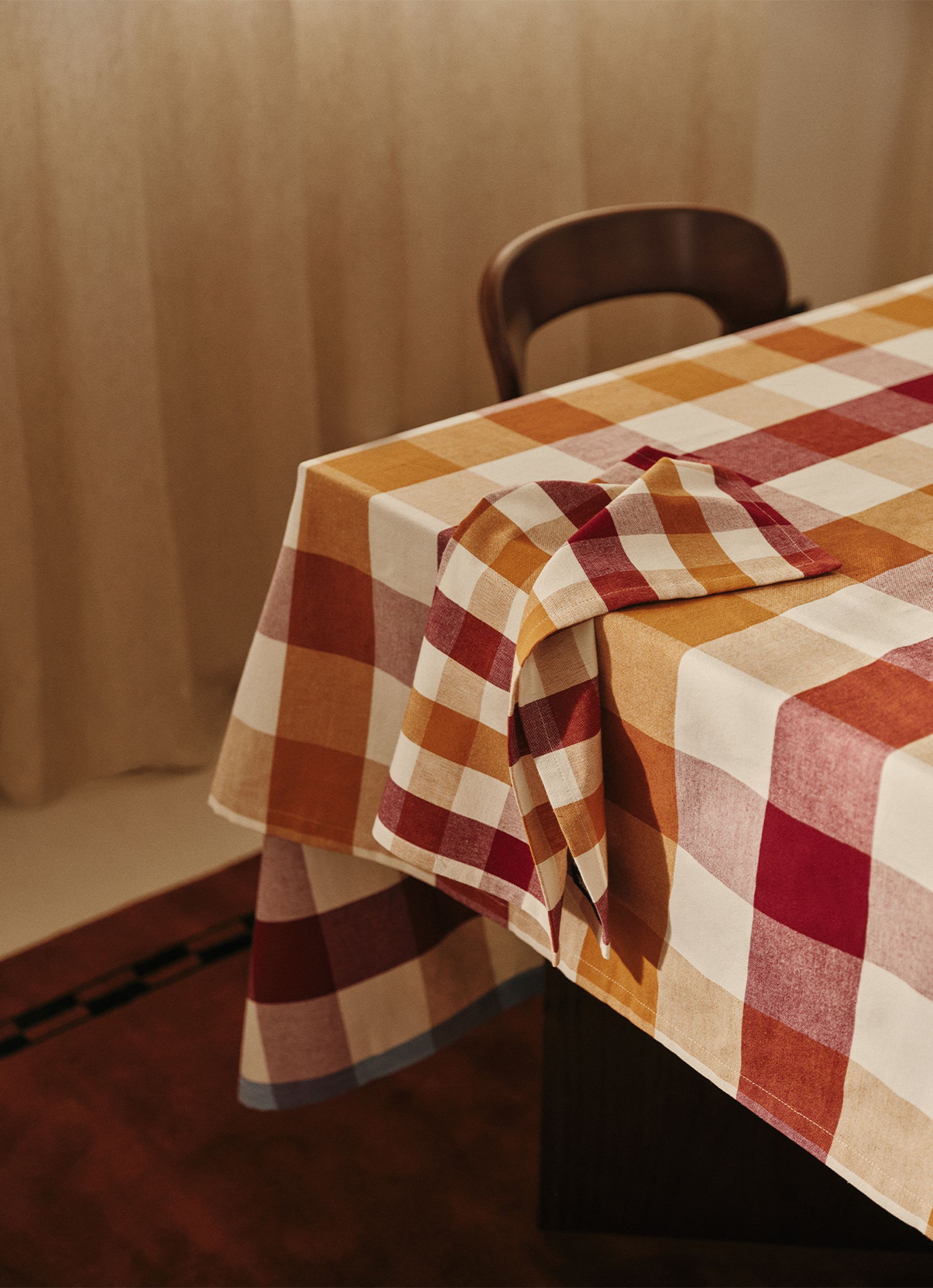Une nappe à carreaux dans les tons de rouge, d'orange et de blanc, avec une serviette soigneusement pliée posée sur le bord d'une chaise en bois.