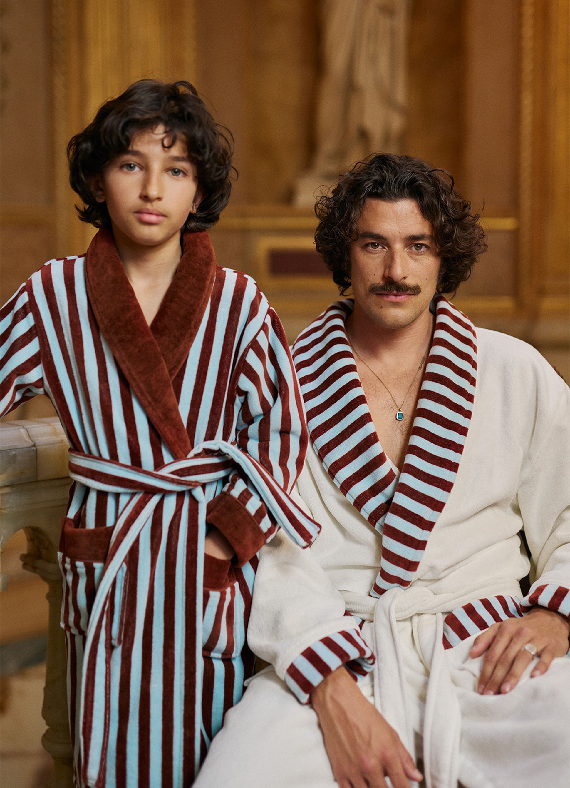 Deux personnes vêtues de peignoirs rayés assortis, assises dans une pièce dont le décor est somptueux.