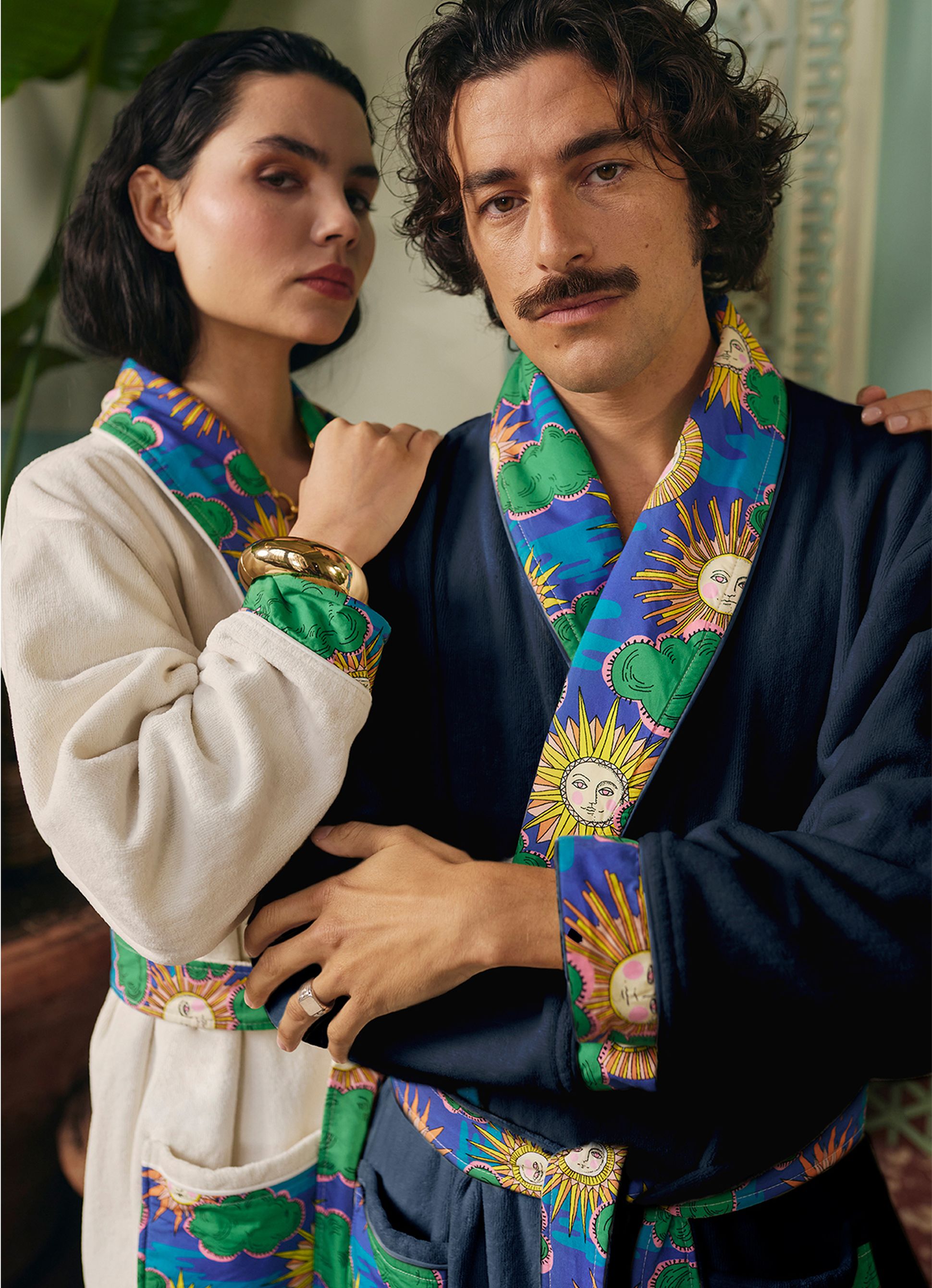 Un homme et une femme, vêtus de peignoirs aux couleurs vives sur le thème du ciel, posent à l'intérieur, rayonnant d'élégance et d'assurance.