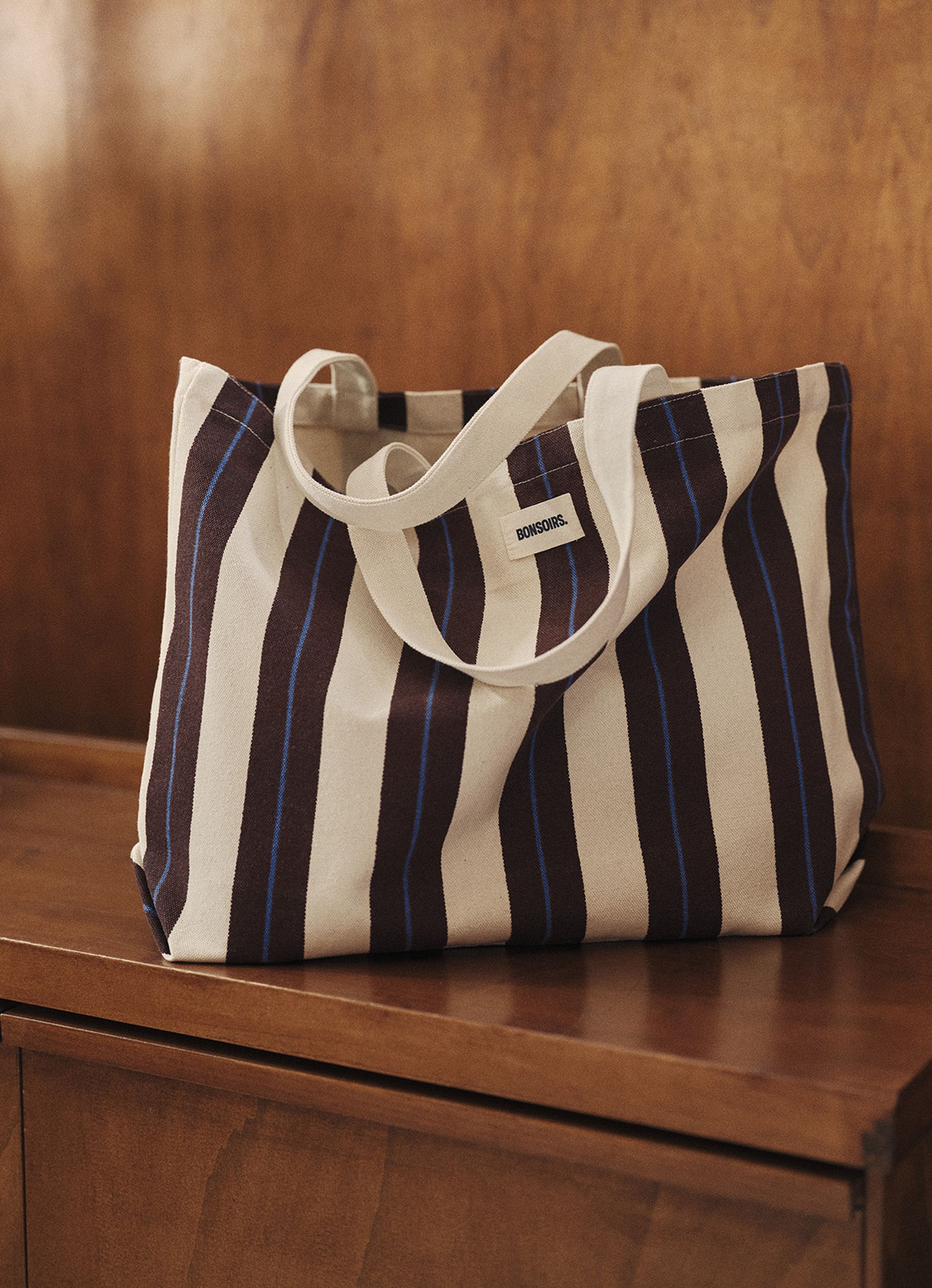 Un sac fourre-tout en toile à rayures verticales claires et foncées repose sur une surface en bois.
