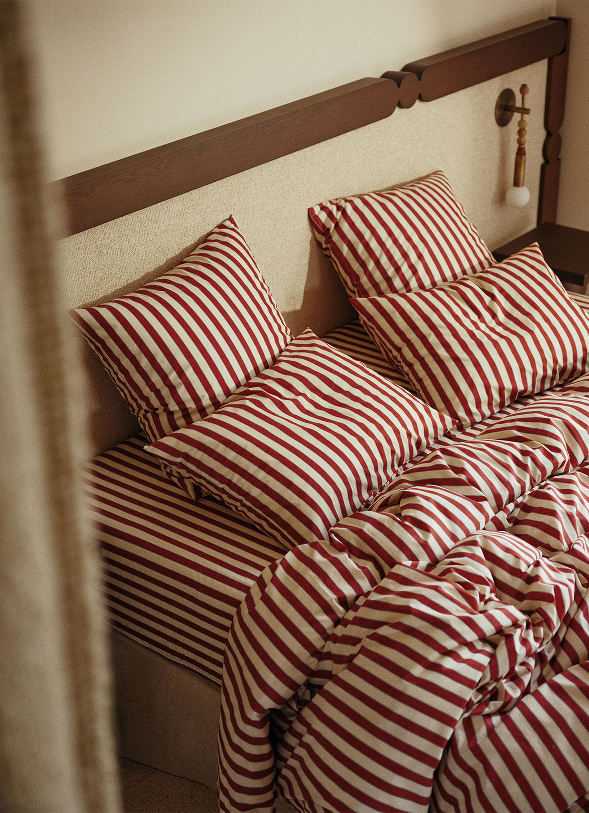 Un lit douillet avec une parure de lit à rayures rouges et blanches, où les oreillers sont soigneusement disposés contre une tête de lit en bois.