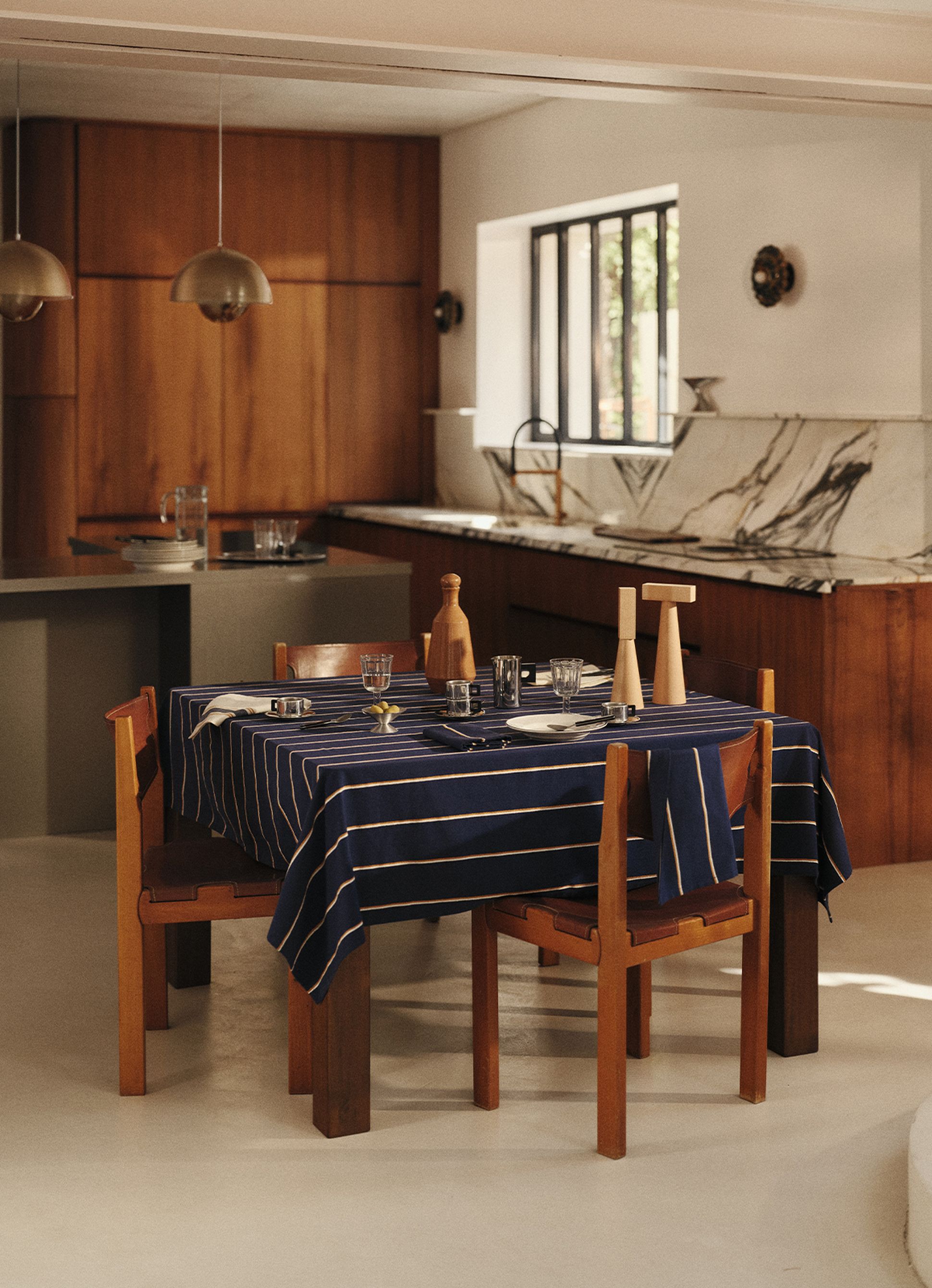 Une salle à manger moderne avec une table en bois dressée sur une nappe bleue rayée, entourée de chaises en bois, et un plan de travail en marbre en arrière-plan.