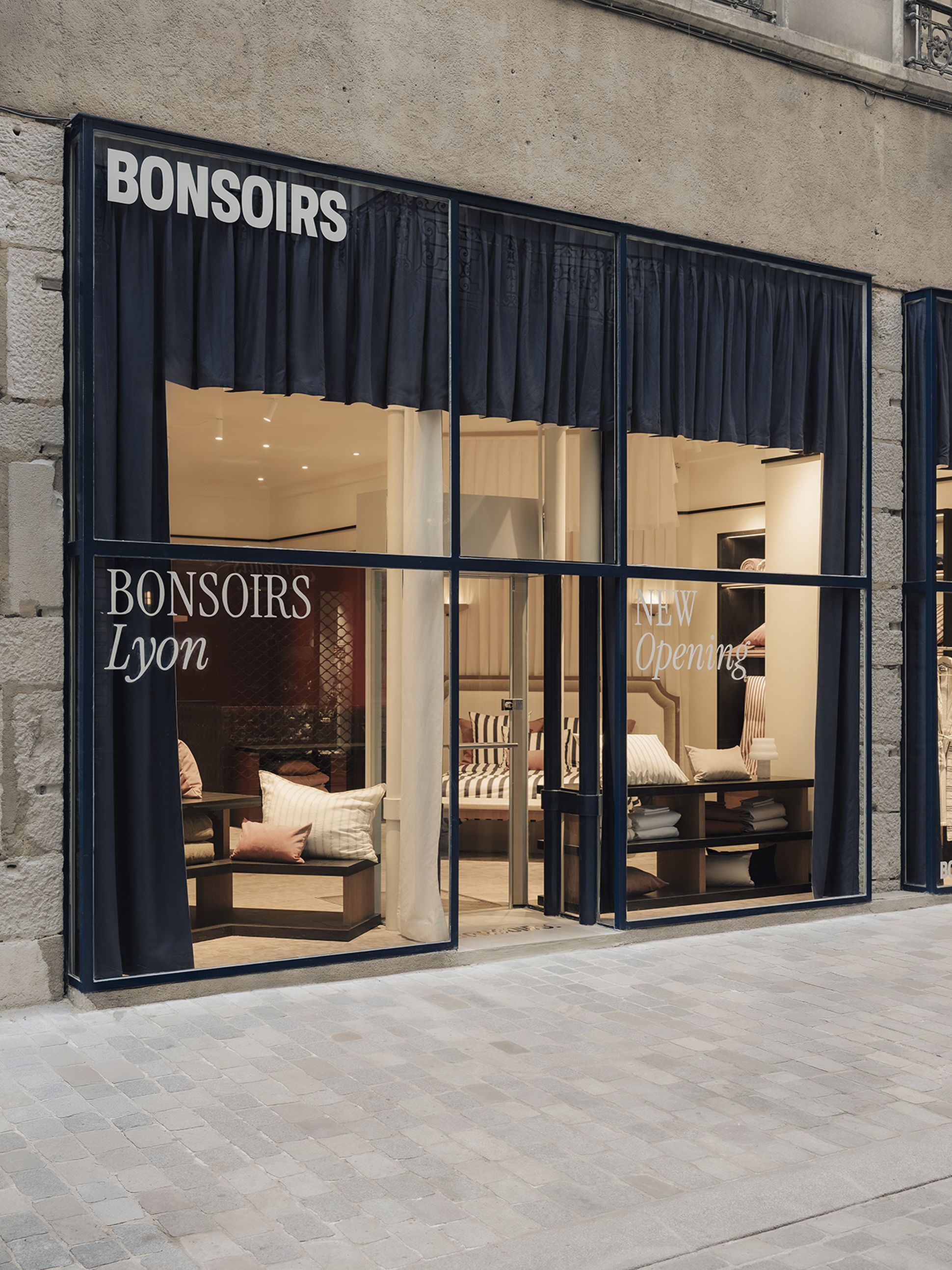 Vitrine arborant l'enseigne « BONSOIRS », dévoilant un intérieur chaleureux avec des coussins rayés et des sièges accueillants à Lyon. Des affiches annoncent une nouvelle ouverture.