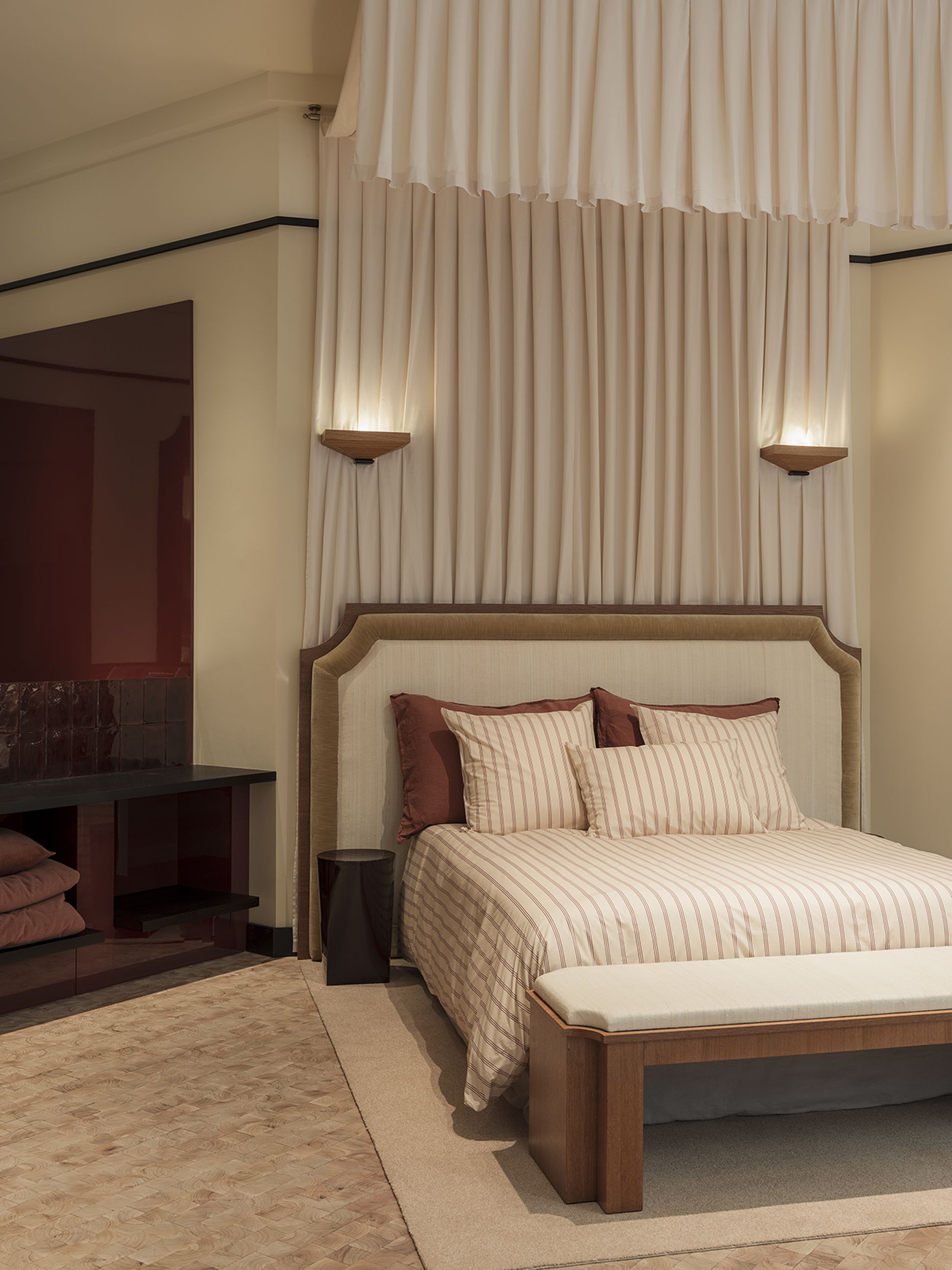 Une chambre élégante avec un couvre-lit rayé, un banc rembourré, des rideaux suspendus, un éclairage tamisé et une ambiance chaleureuse.
