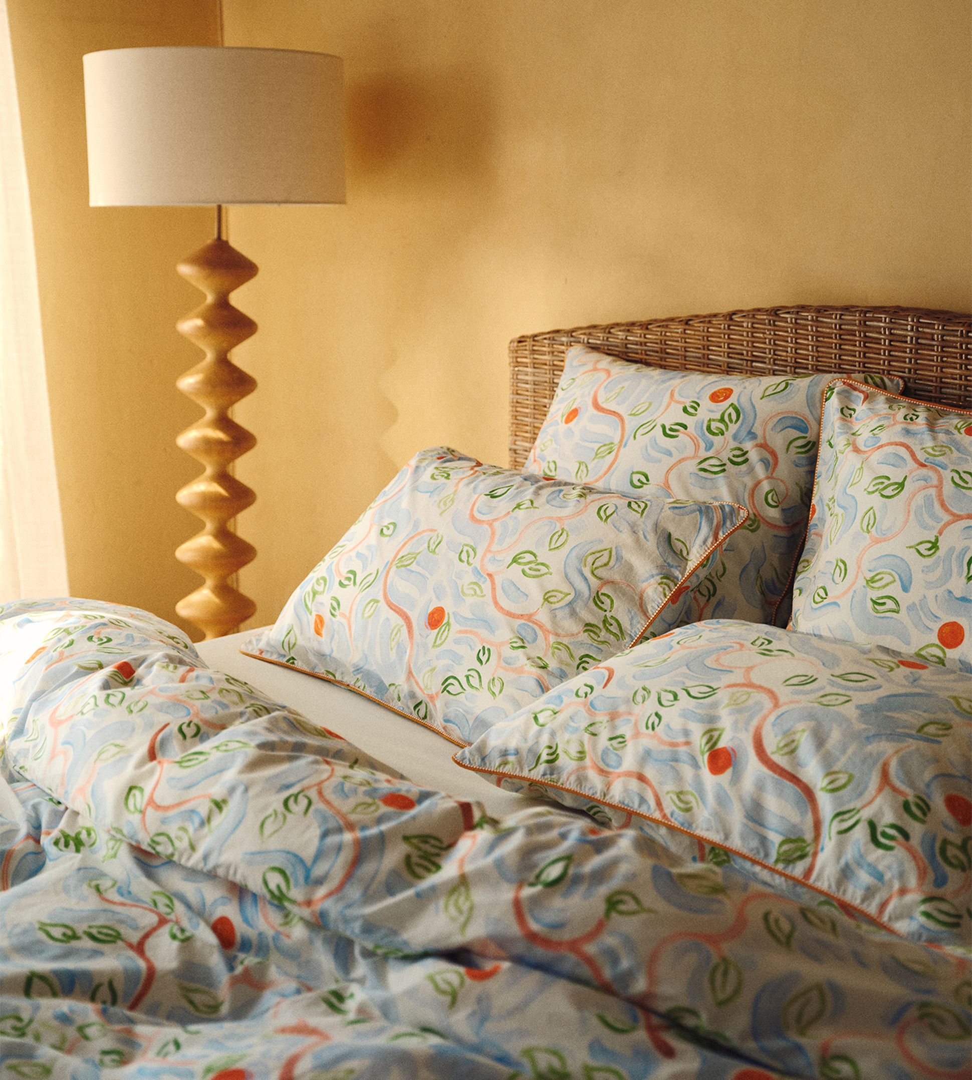 Une chambre douillette avec un lit à tête de lit en osier, une parure de lit aux motifs colorés et une élégante lampe en bois posée à côté.