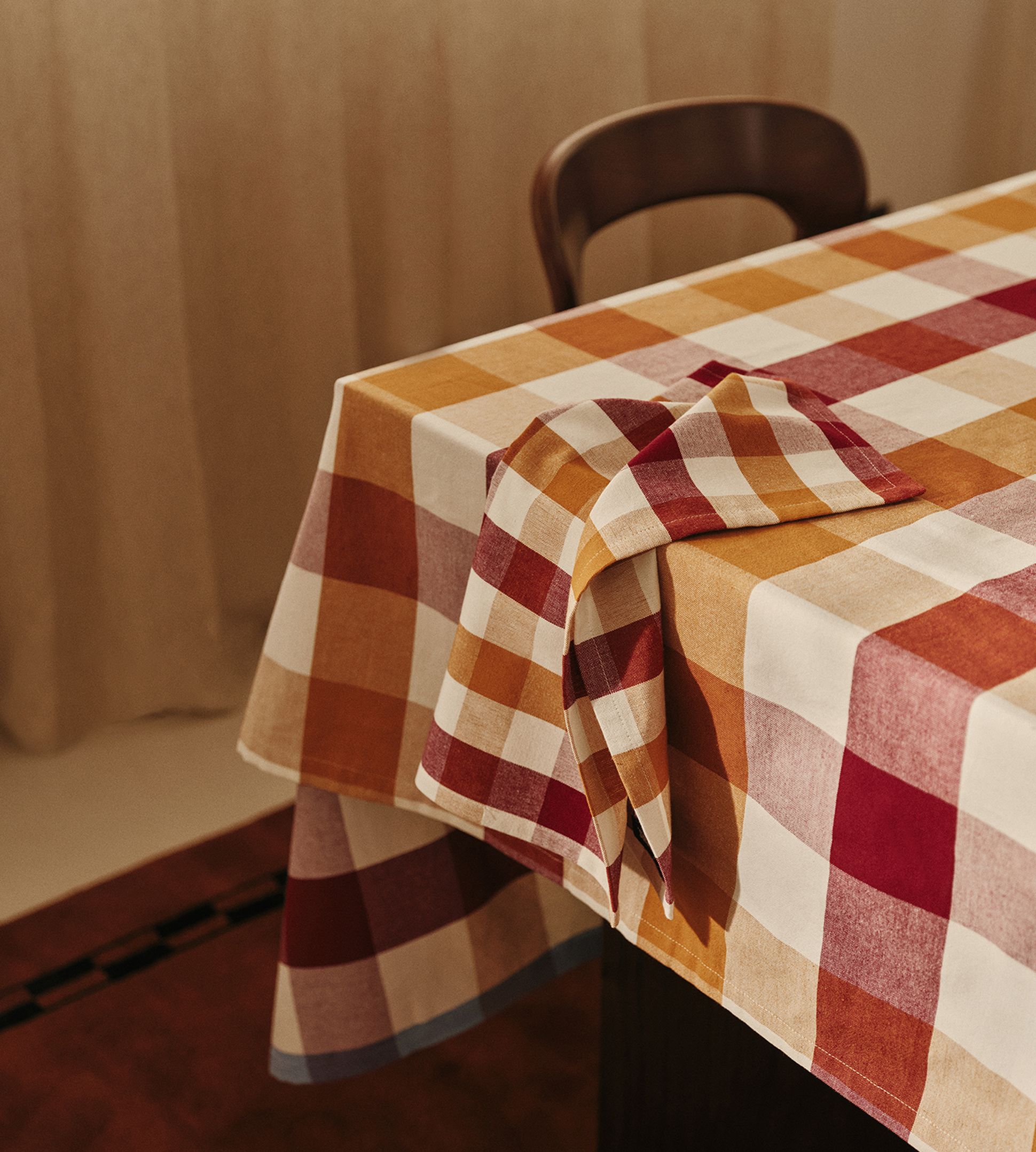 Une nappe à carreaux dans des tons de rouge, d'orange et de beige recouvre une table, avec une serviette pliée assortie.