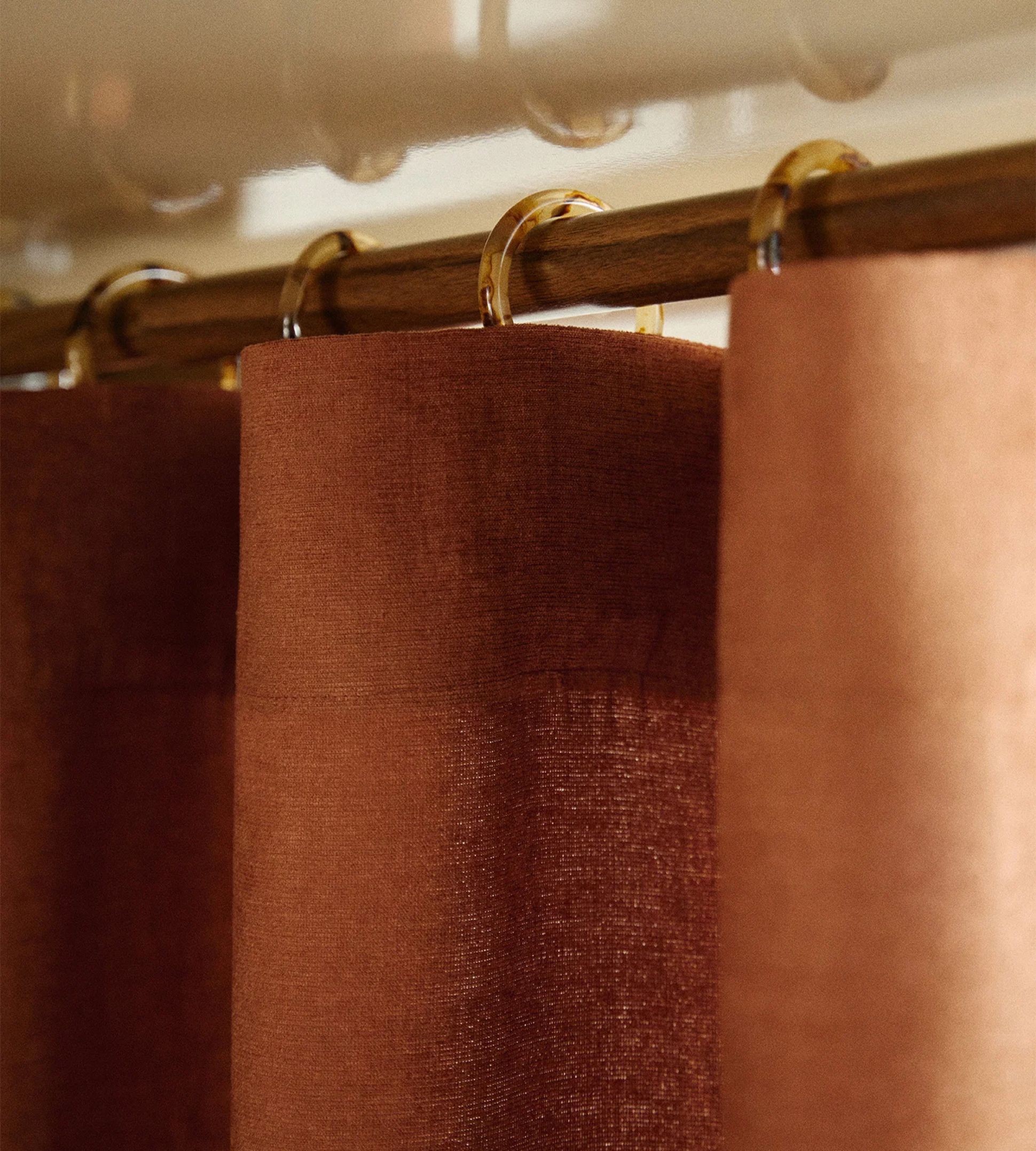 Gros plan sur des rideaux marron suspendus à une tringle en bois à l'aide d'anneaux transparents.